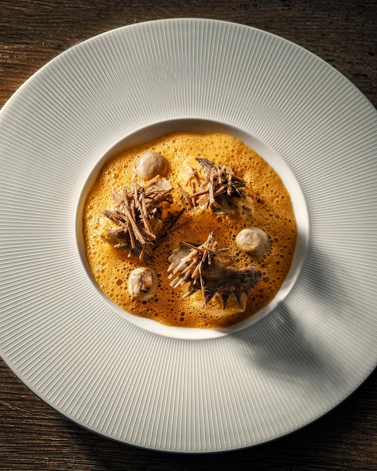 Gourmet truffle dish by Chef Alain Parodi at Veritable, featuring black truffle shavings and golden foam on Pillivuyt porcelain. Professional food photography by Stavros Kostakis using dramatic Rembrandt lighting