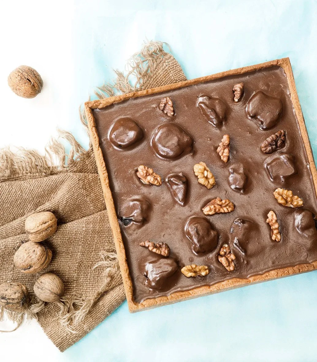Overhead editorial shot of a chocolate walnut tart on a rustic setup, highlighting food styling and artisanal baking ingredients.