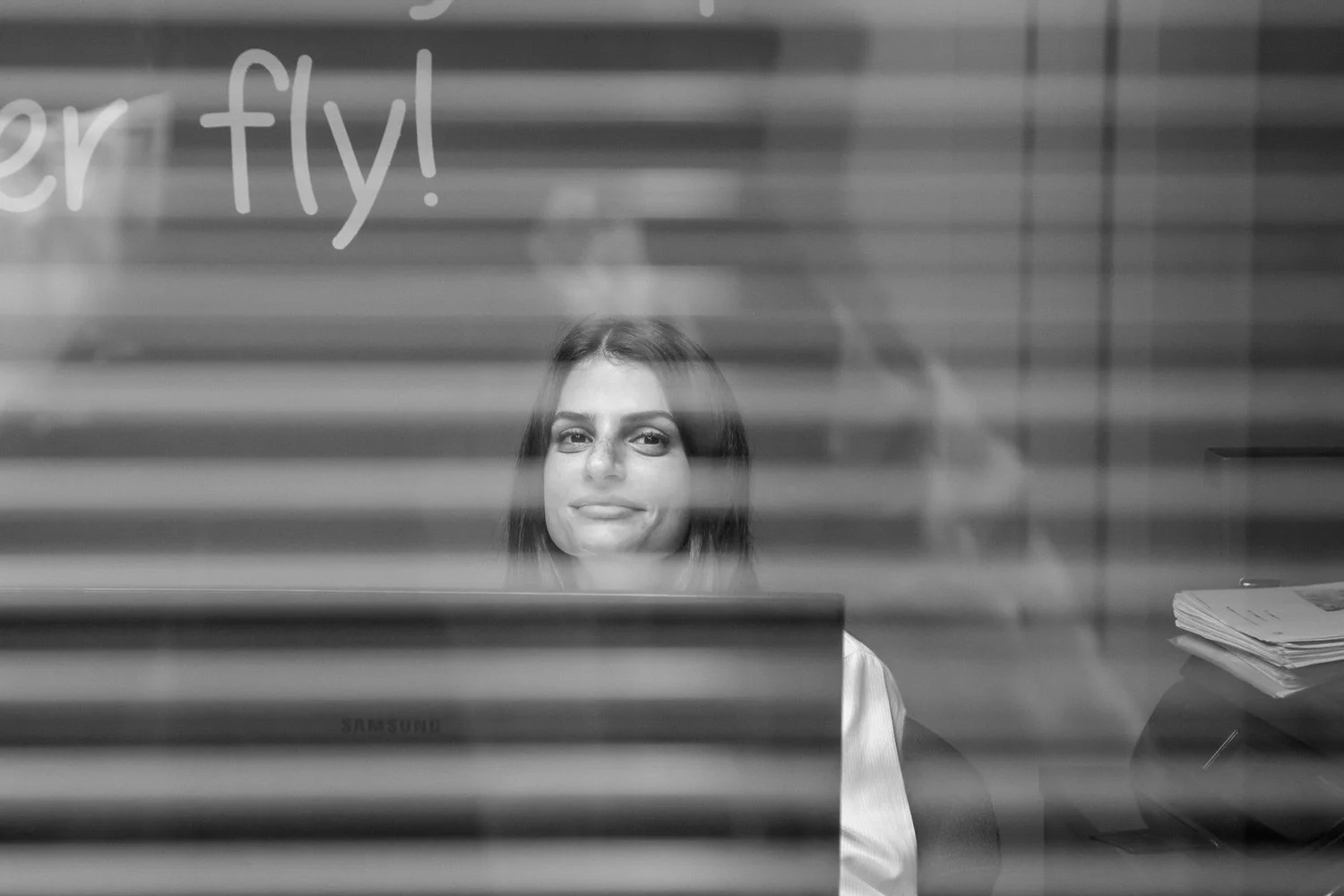 Cinematic black and white environmental portrait of Marita Simoneti, captured through office blinds for a documentary aesthetic. A creative corporate character study by Stavros Kostakis that emphasizes professional atmosphere and modern office storyt