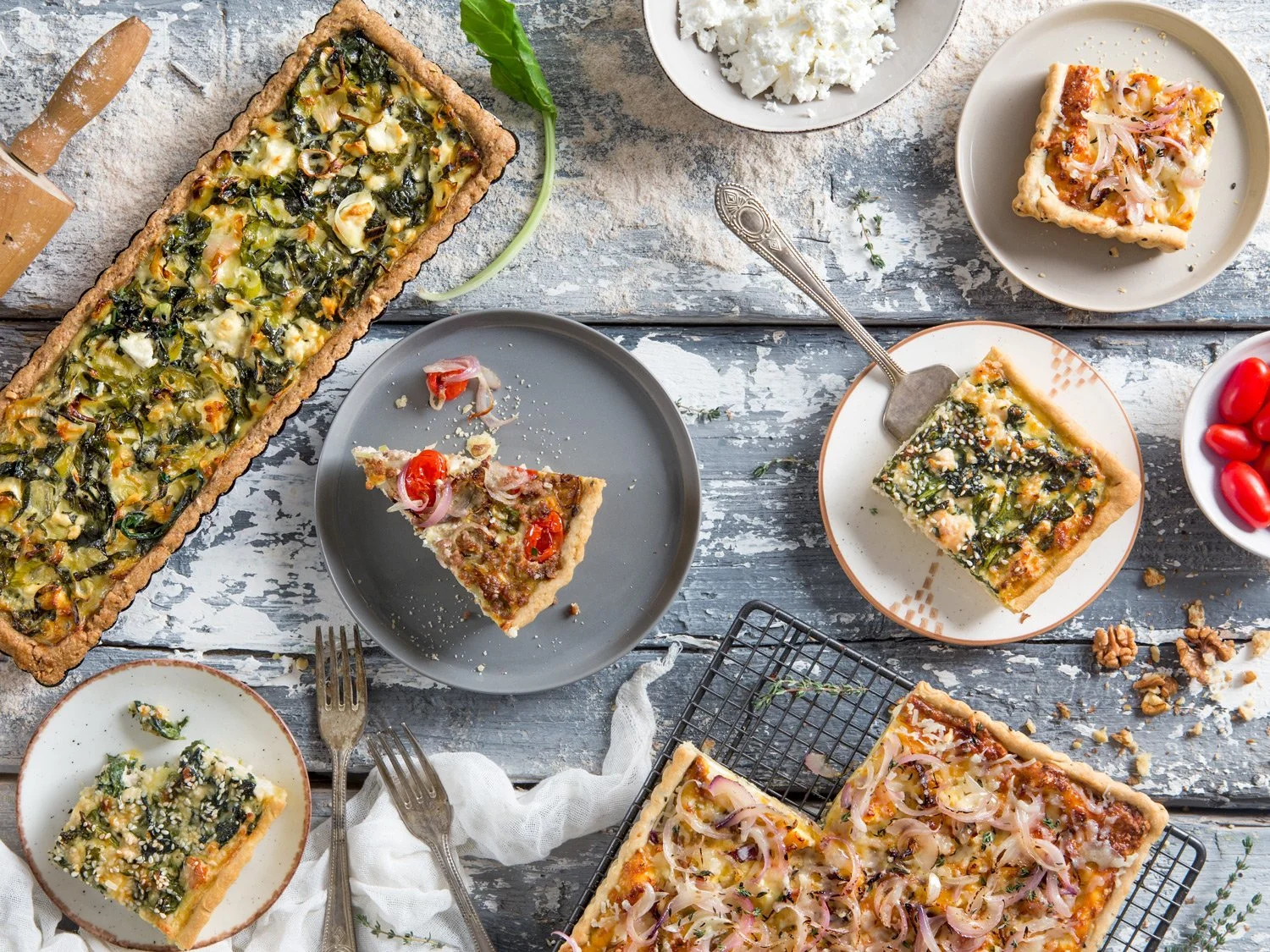 Professional flat lay food photography of rustic savory tarts with spinach and cheese on a grey wooden background, by Stavros Kostakis.