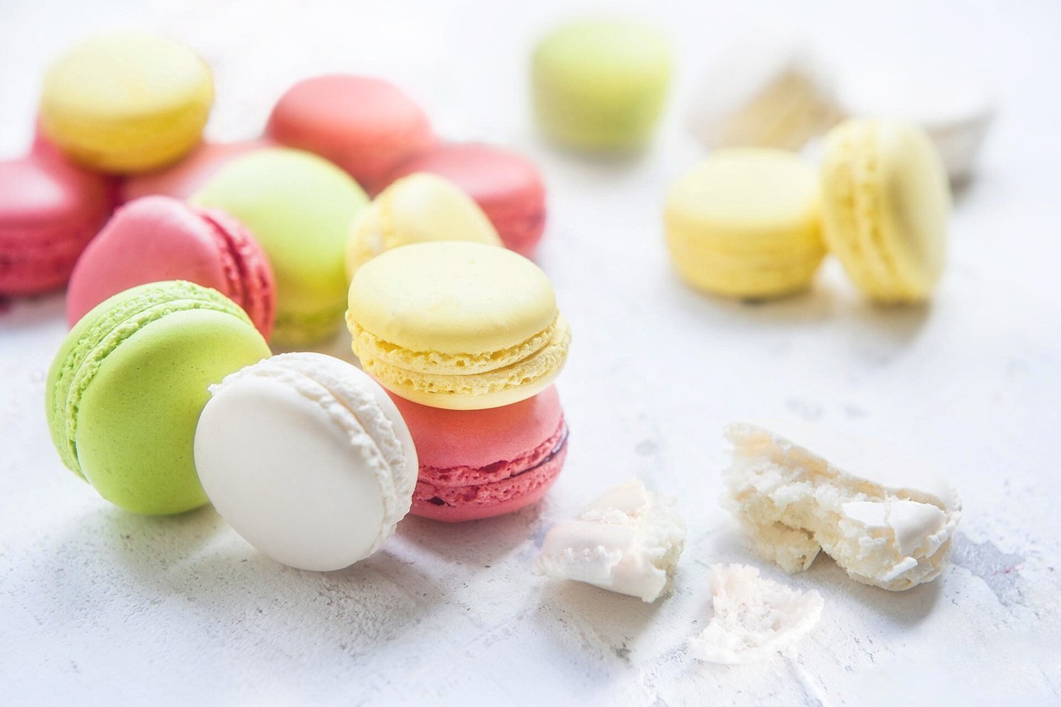 Bright high-key food photography of colorful French macarons on a white textured background, highlighting the delicate crust and soft colors, by Stavros Kostakis.
