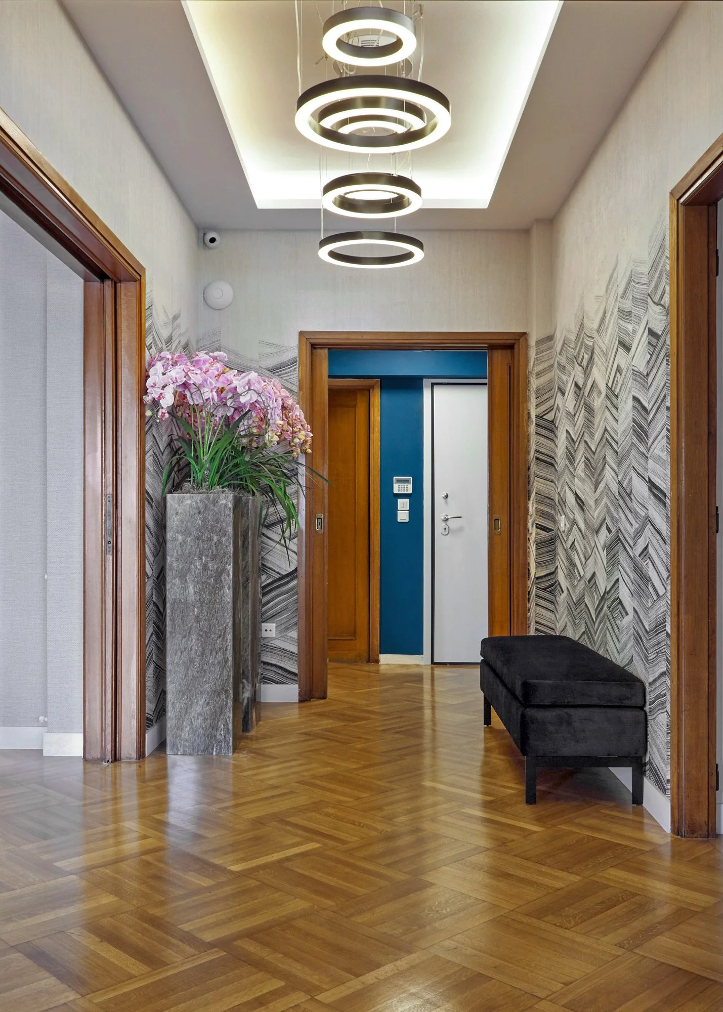 Interior photography of a hallway in a Kolonaki law firm, designed by Sissy Feida. Highlights include a dramatic chevron-patterned wallpaper, modern circular LED pendant lights, and a luxury velvet bench. Captured by Stavros Kostakis.