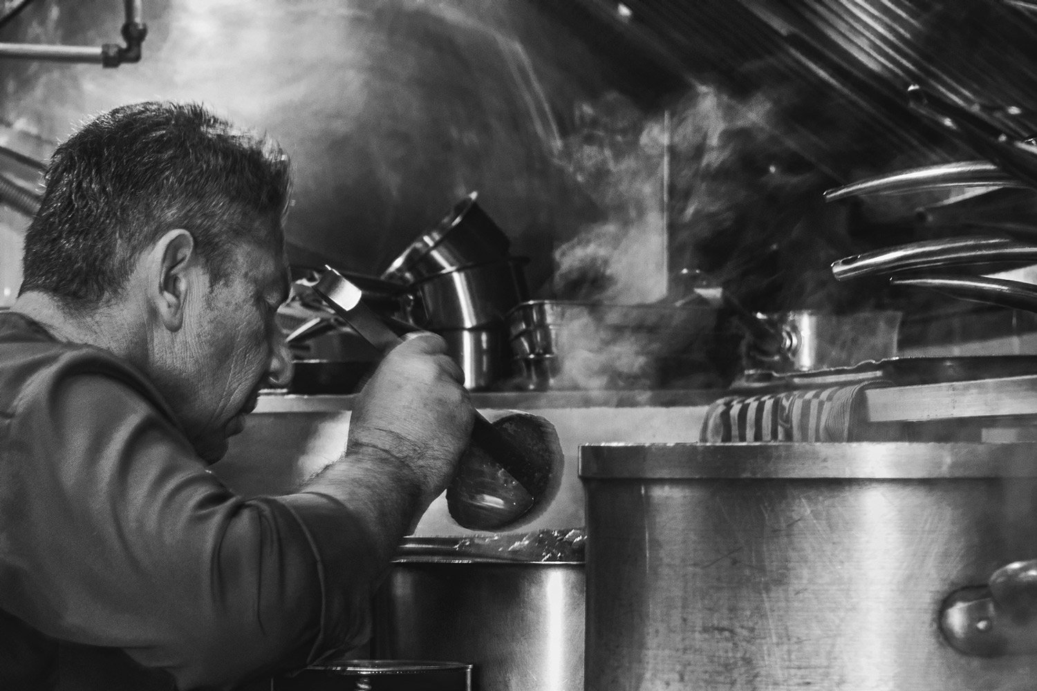 Veri table ,Alain Parodi Professional kitchen action shot captured by Stavros Kostakis, featuring a chef in his element. A black and white documentary-style photograph emphasizing the intensity, steam, and craftsmanship behind high-end culinary creat