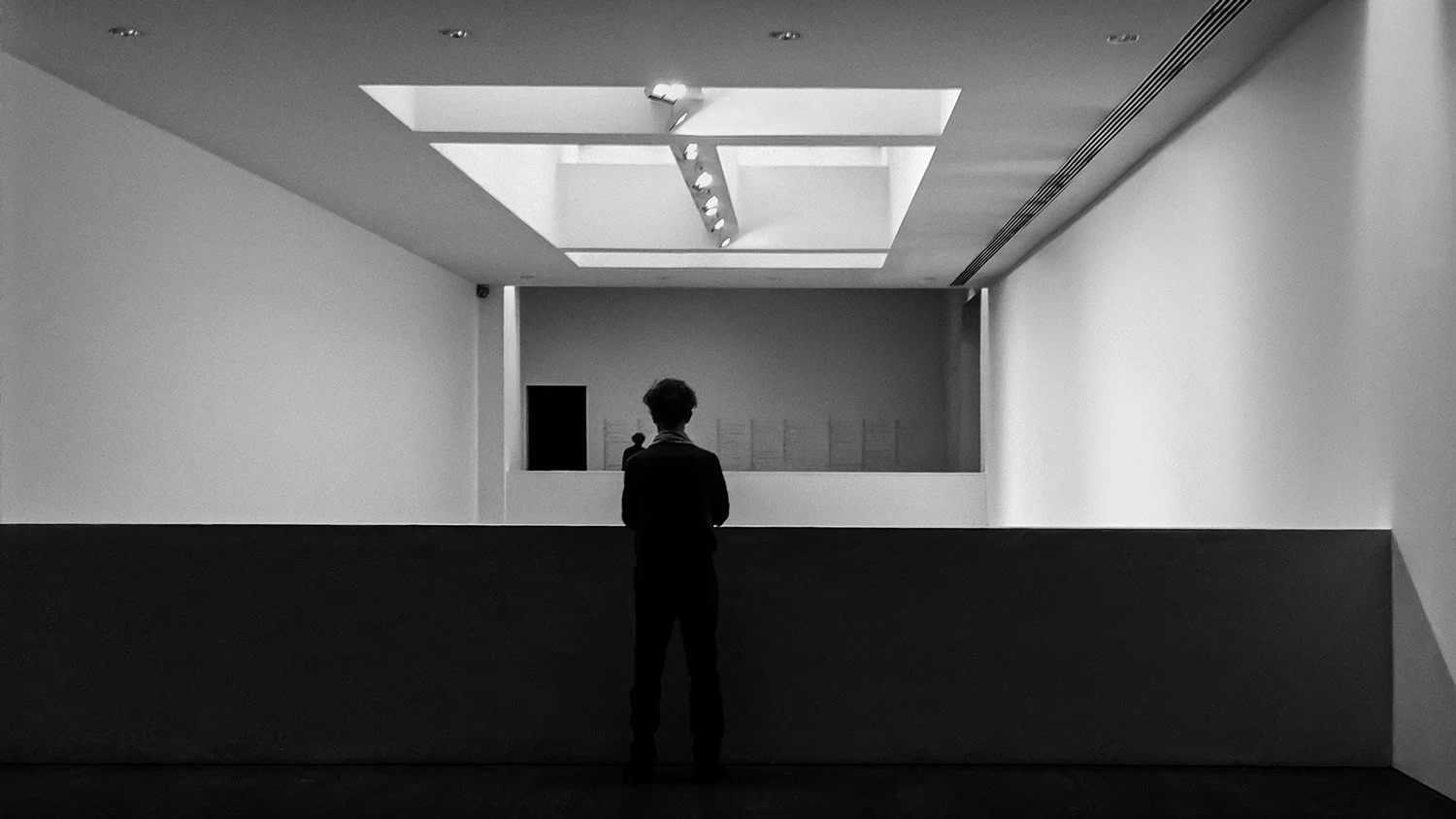 Black and white fine art photography of a silhouette overlooking a minimalist museum interior at S.M.A.K. Ghent, Belgium, representing the 'Art of Perception' by Stavros Kostakis.