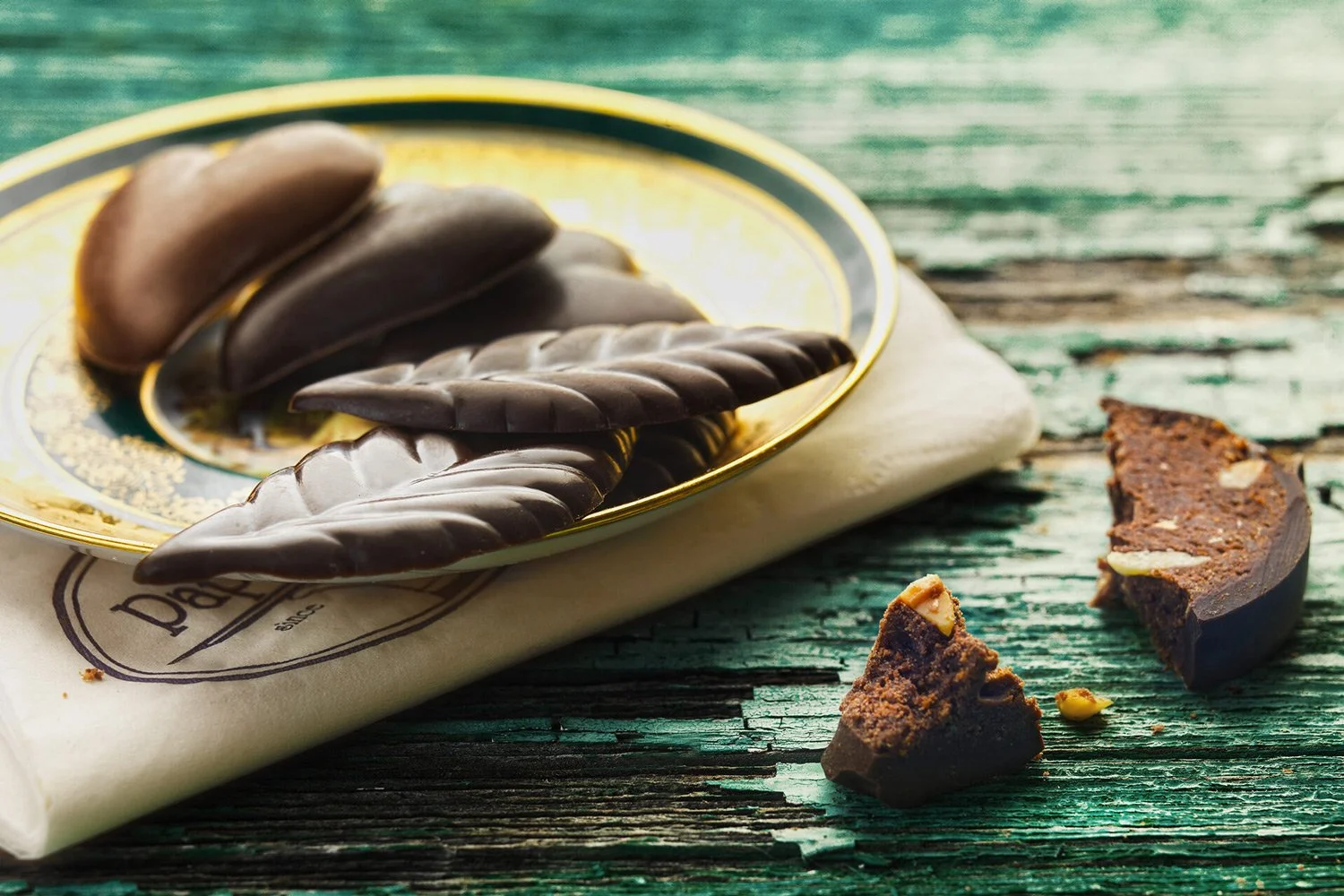 Editorial food photography of handmade chocolate leaves and pralines for Papaspirou confectionery, set on a rustic wooden background with vintage plating, by Stavros Kostakis.