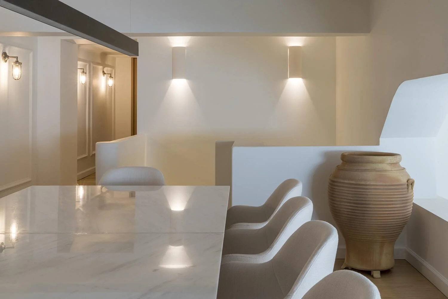 A cinematic interior detail of the Papaioannou restaurant, showcasing the contrast between a smooth, reflective marble table and a large traditional terracotta vessel. The composition highlights the fusion of contemporary minimalism with rustic eleme