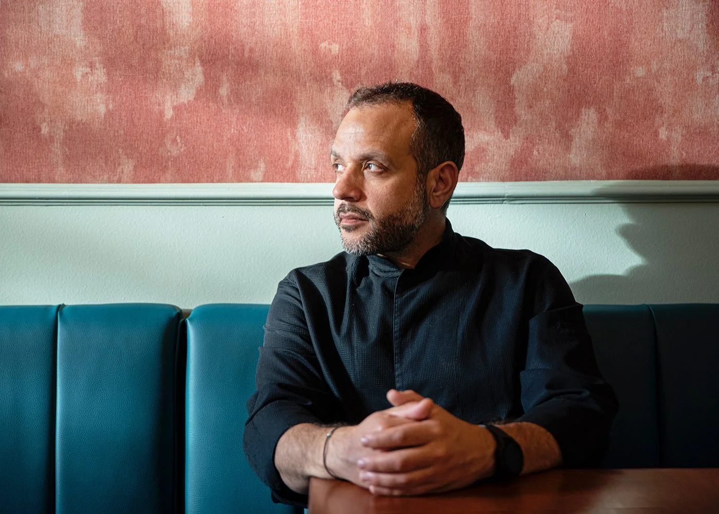 Sophisticated color portrait of Chef Giannis Liokas in a contemporary restaurant interior. Captured by Stavros Kostakis, the image features a warm, textured background and a thoughtful, candid expression, highlighting professional personality and mod