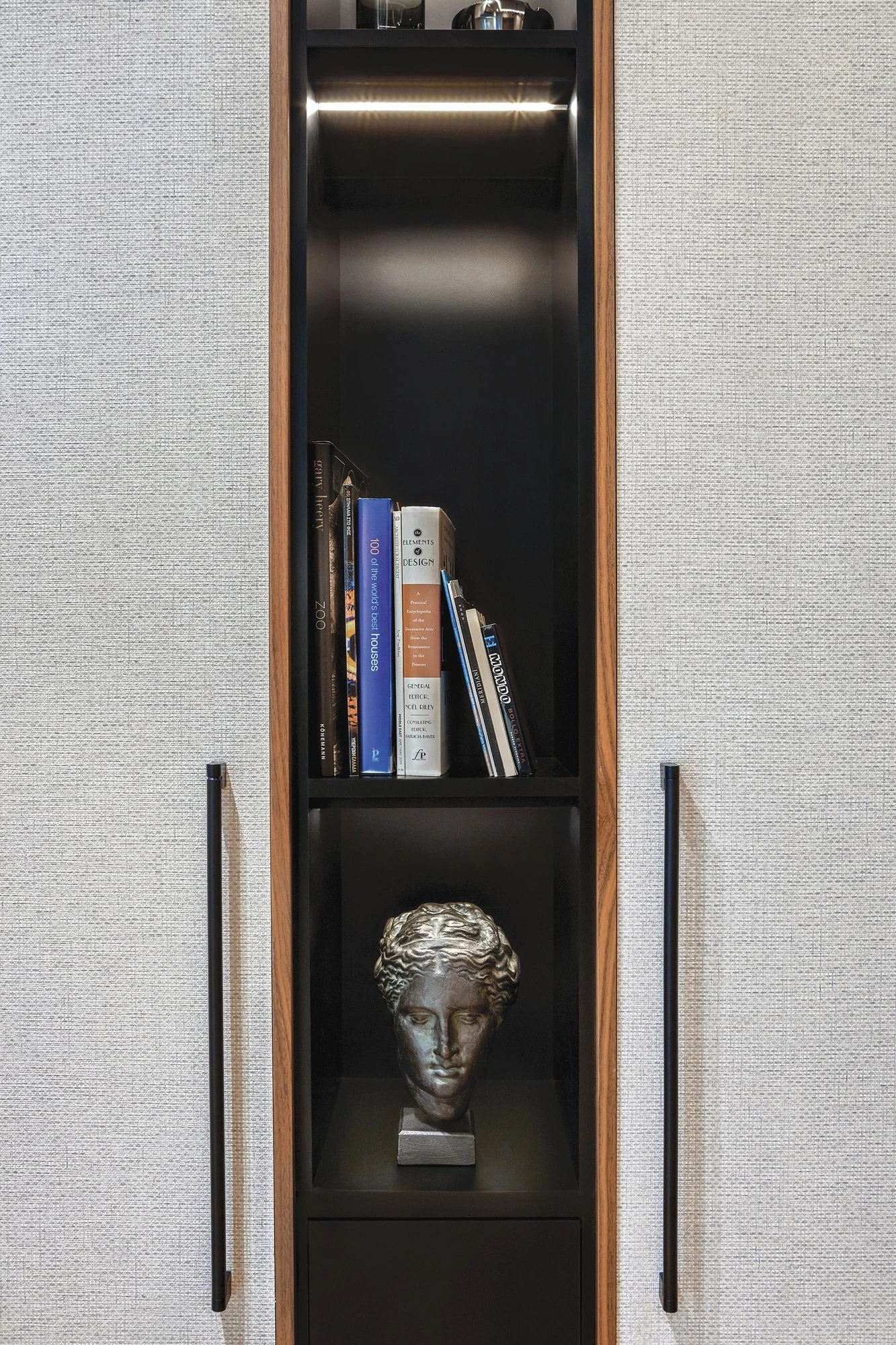 Symmetrical interior detail shot of a custom-built office library. Features integrated lighting, textured wallcovering, and a classic bust sculpture, curated by Sissy Feida. Photographed by Stavros Kostakis.