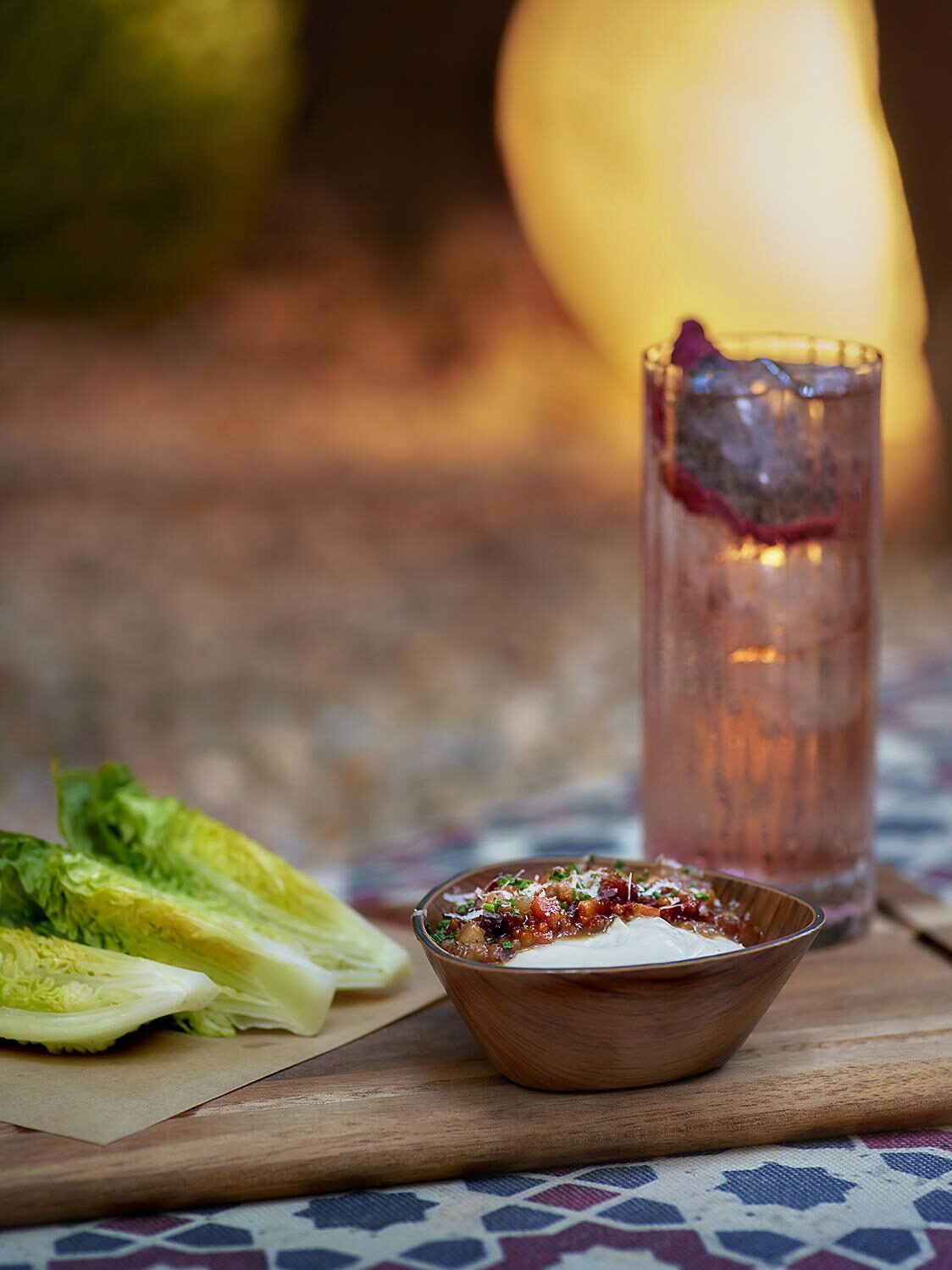 Editorial food and cocktail pairing at Hide & Seek. A close-up of a gourmet appetizer with lettuce hearts, accompanied by a signature pink cocktail in a highball glass with dramatic backlighting.