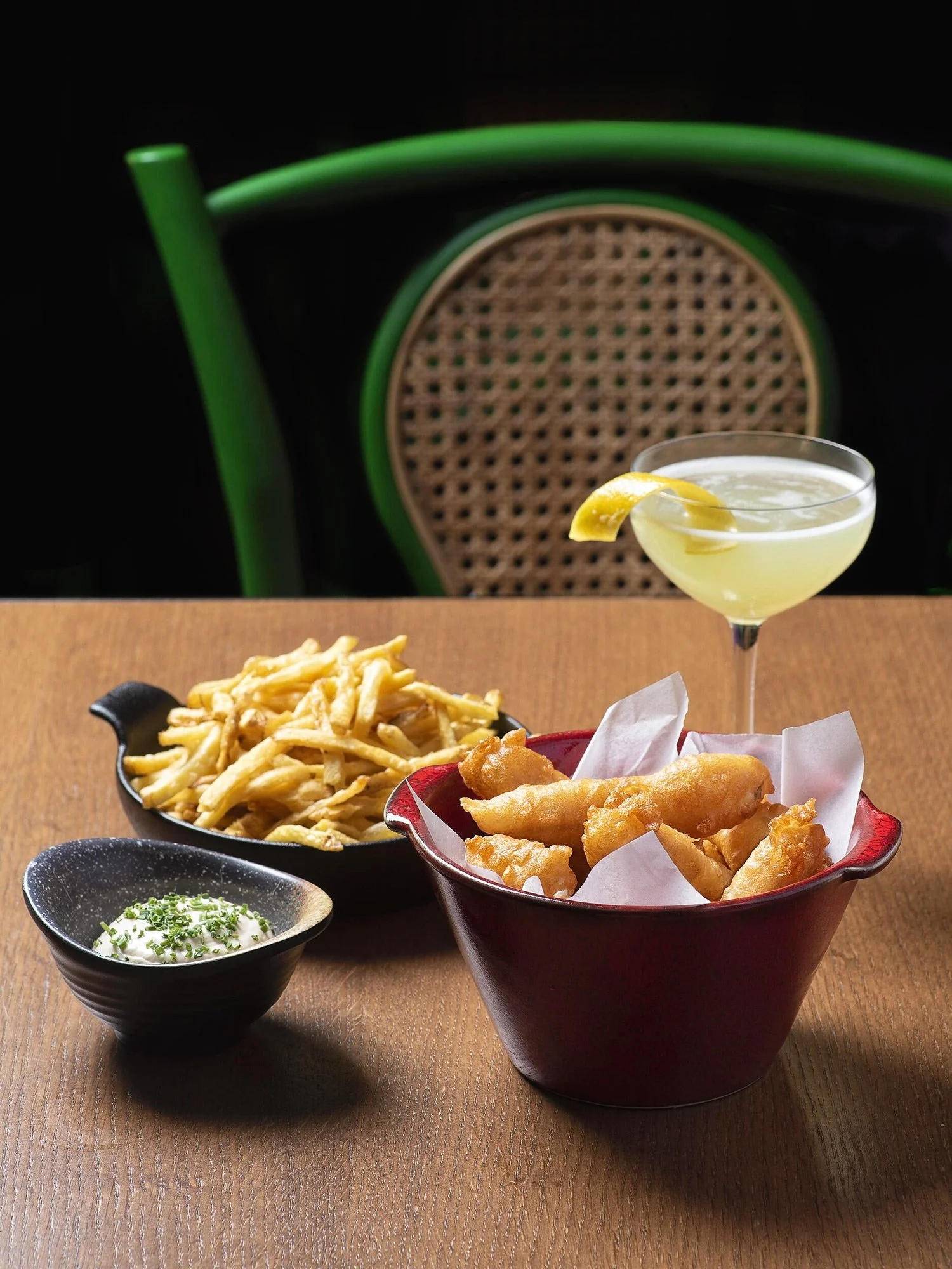 Crispy tempura shrimps served in a red bowl with a side of truffle fries and a classic citrus cocktail. Shot against a rustic wooden table and a signature green bistro chair at Royal Monkey Kifisia. Captured by Stavros Kostakis.
