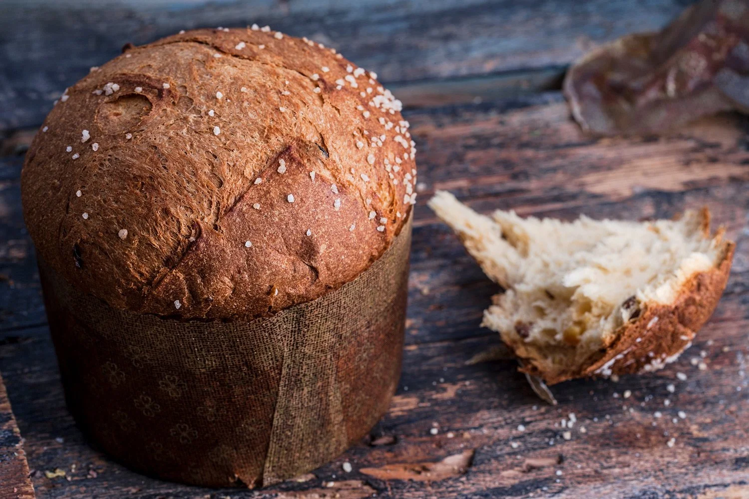 Commercial styling & food photography for Papaspirou Bakery  of a traditional handmade Panettone on a rustic wooden background, featuring pearl sugar topping and a detailed view of its airy, artisan texture.