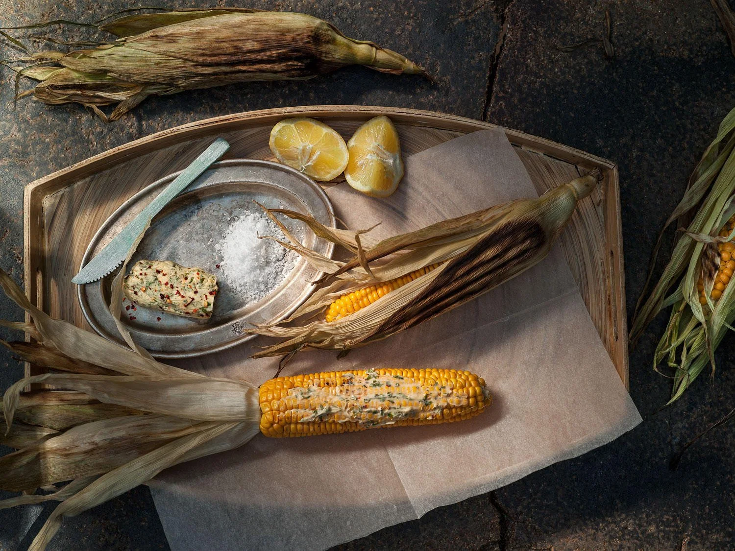 Argiro Barbarigou Cookbooks | Editorial Gastronomy. Editorial food photography for Argiro Barbarigou's cookbooks, featuring roasted corn with herb butter on a rustic tray, by Stavros Kostakis.