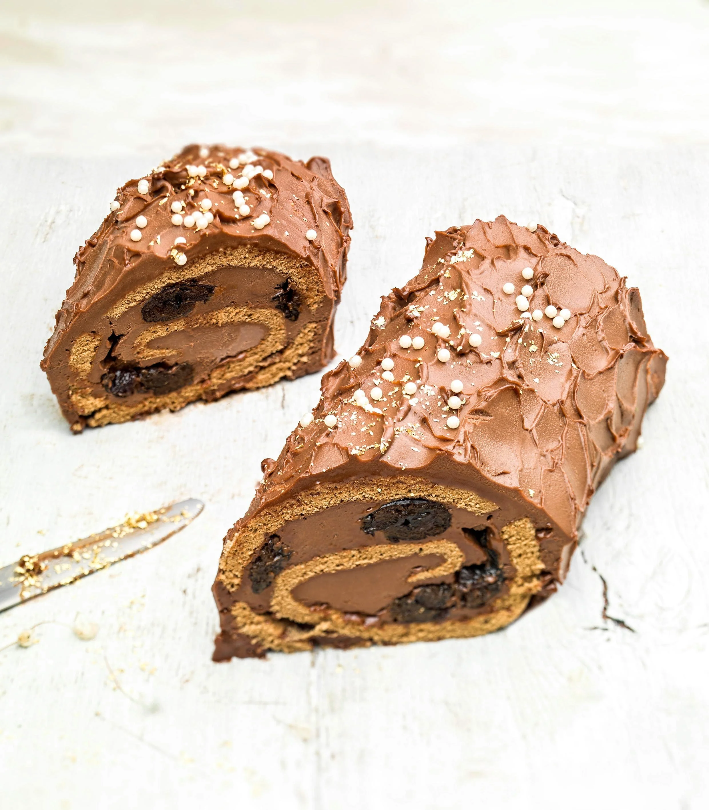 Professional styling & pastry photography for Evita Papacharalampous featuring a premium chocolate roll with gold flakes and white pearl sugar, presented on a bright, minimalist surface for high-end patisserie branding.