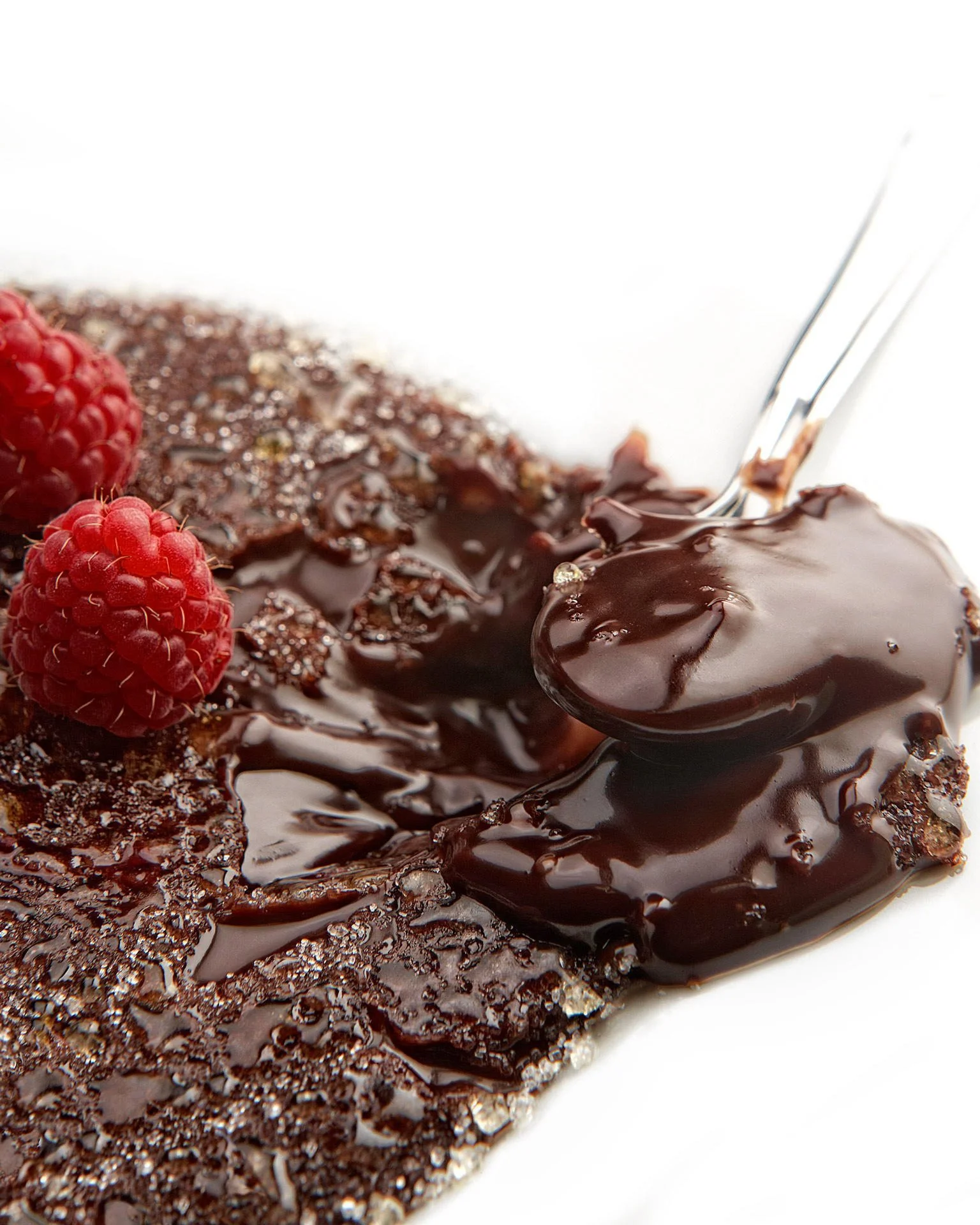 Decadent chocolate ganache with fresh raspberries and shattered sugar crystals—culinary photography by Stavros Kostakis