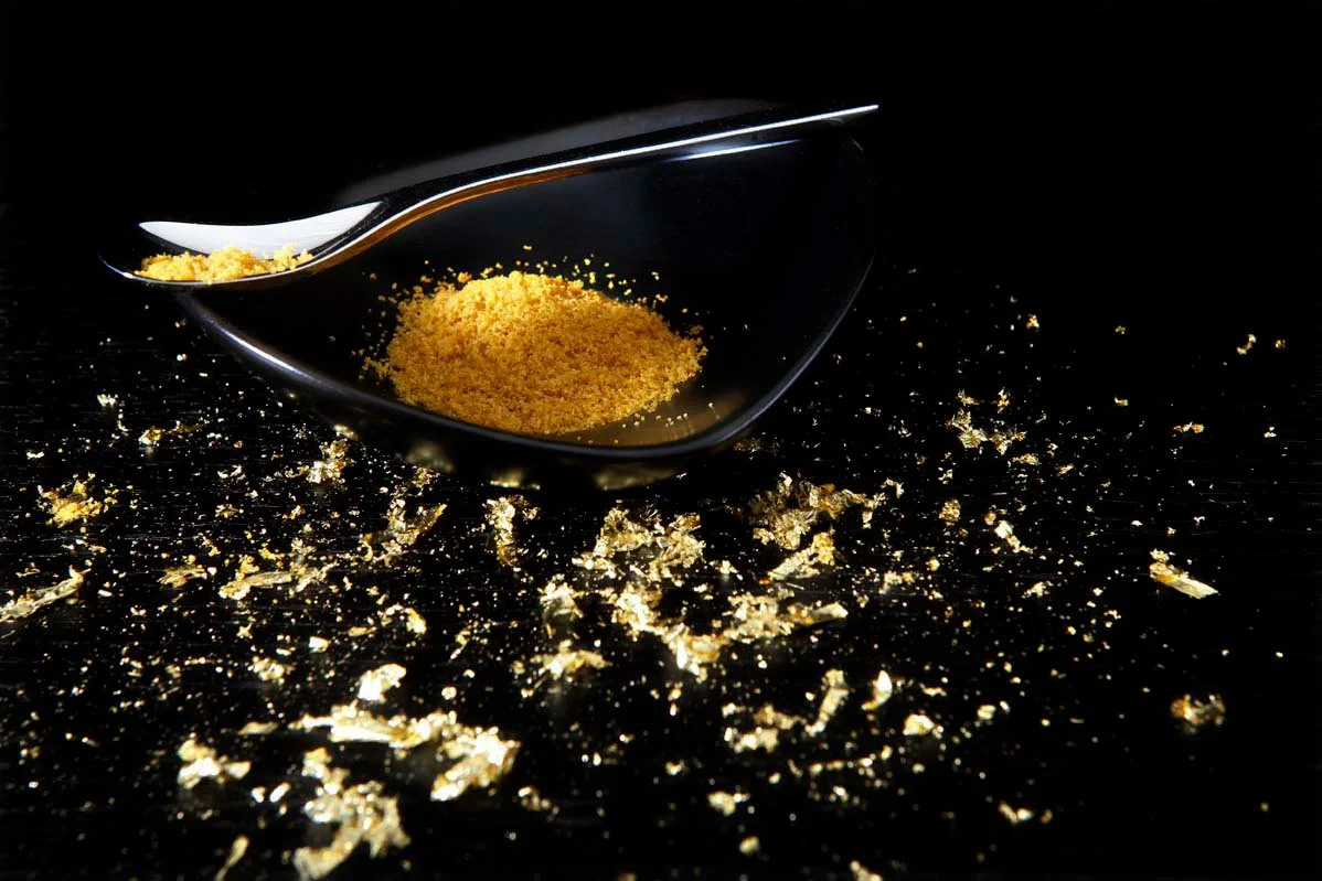 Luxury food photography by Stavros Kostakis featuring Trikalinos Bottarga powder in a black bowl surrounded by edible gold flakes.