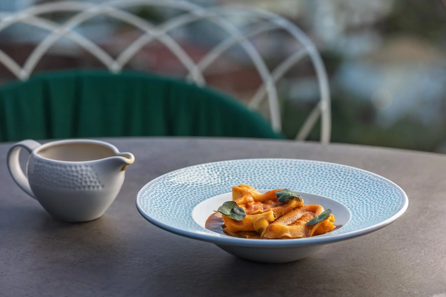 Fine dining atmosphere at Four Elements restaurant, Irida Hotel, Parga, with a stunning view of the Ionian Sea. Mediterranean gourmet pasta with deep orange sauce, featuring edible nasturtium leaves, presented with a delicate patterned ceramic plate 