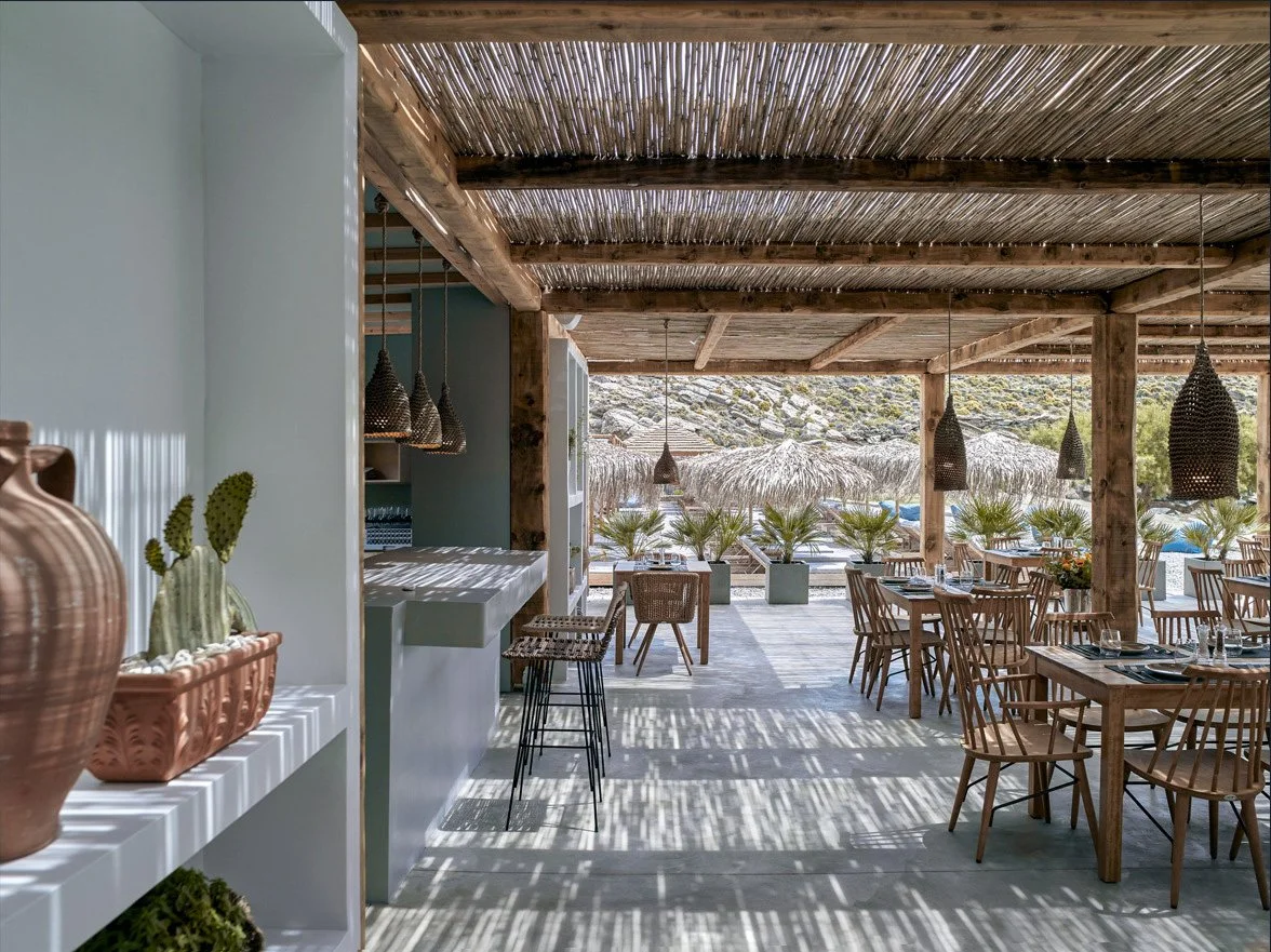Bianco Beach House in Tinos.
 The architectural convergence of stone and wood. The outdoor space of Bianco Beach House in Tinos, with its bamboo pergola and woven lights, creates an atmosphere of sophisticated Cycladic luxury. A series of shots highl