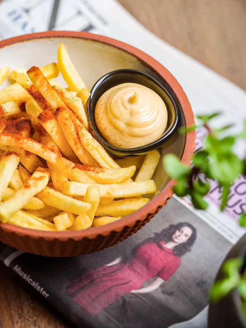 Professional food photography of crispy gourmet fries with paprika and dipping sauce in a terracotta bowl. Shot on location in Utrecht, Netherlands. High-end casual dining aesthetic by Stavros Kostakis.