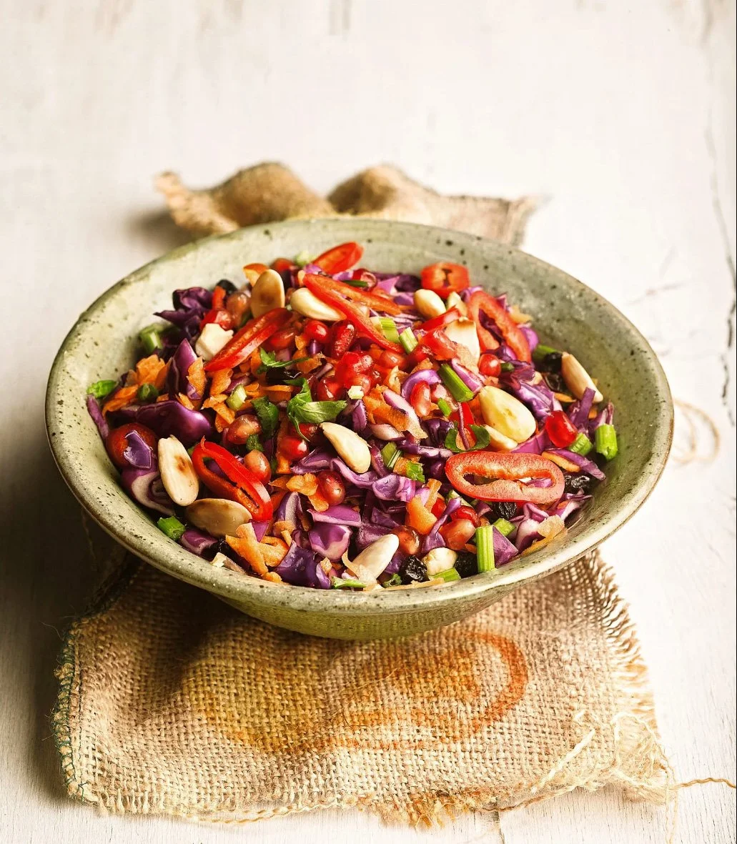 Editorial Archives High-end food photography of a vibrant purple cabbage salad with pomegranate and nuts in a ceramic bowl. Bright, natural lighting.