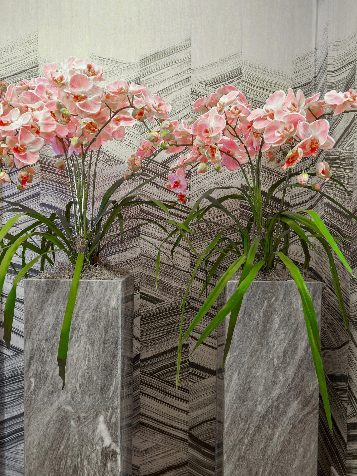 Interior detail shot by Stavros Kostakis featuring custom grey marble pedestals with pink orchids. Set against a textured chevron wallpaper in a luxury Kolonaki office designed by Sissy Feida