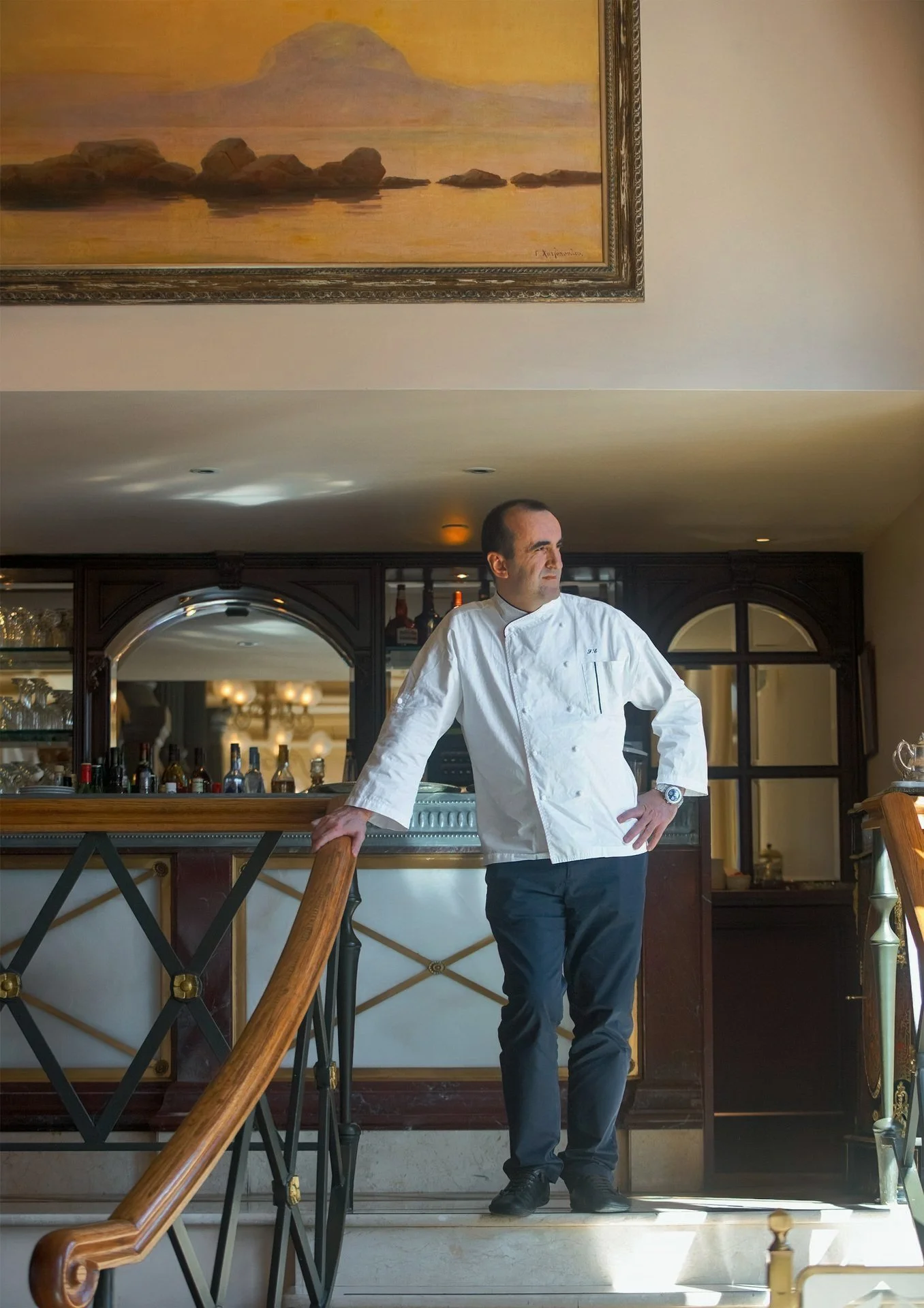 Formal editorial portrait of Executive Chef Sotiris Evagelou posing on the grand marble staircase of Hotel Grande Bretagne. Traditional hospitality style by Stavros Kostakis.