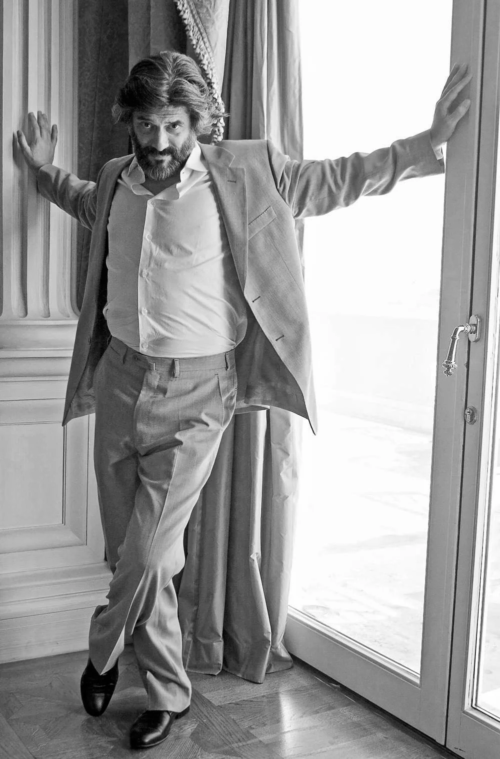 Cinematic, black and white portrait of actor George Chorafas, posing naturally against a large window. High-end editorial photography by Stavros Kostakis.