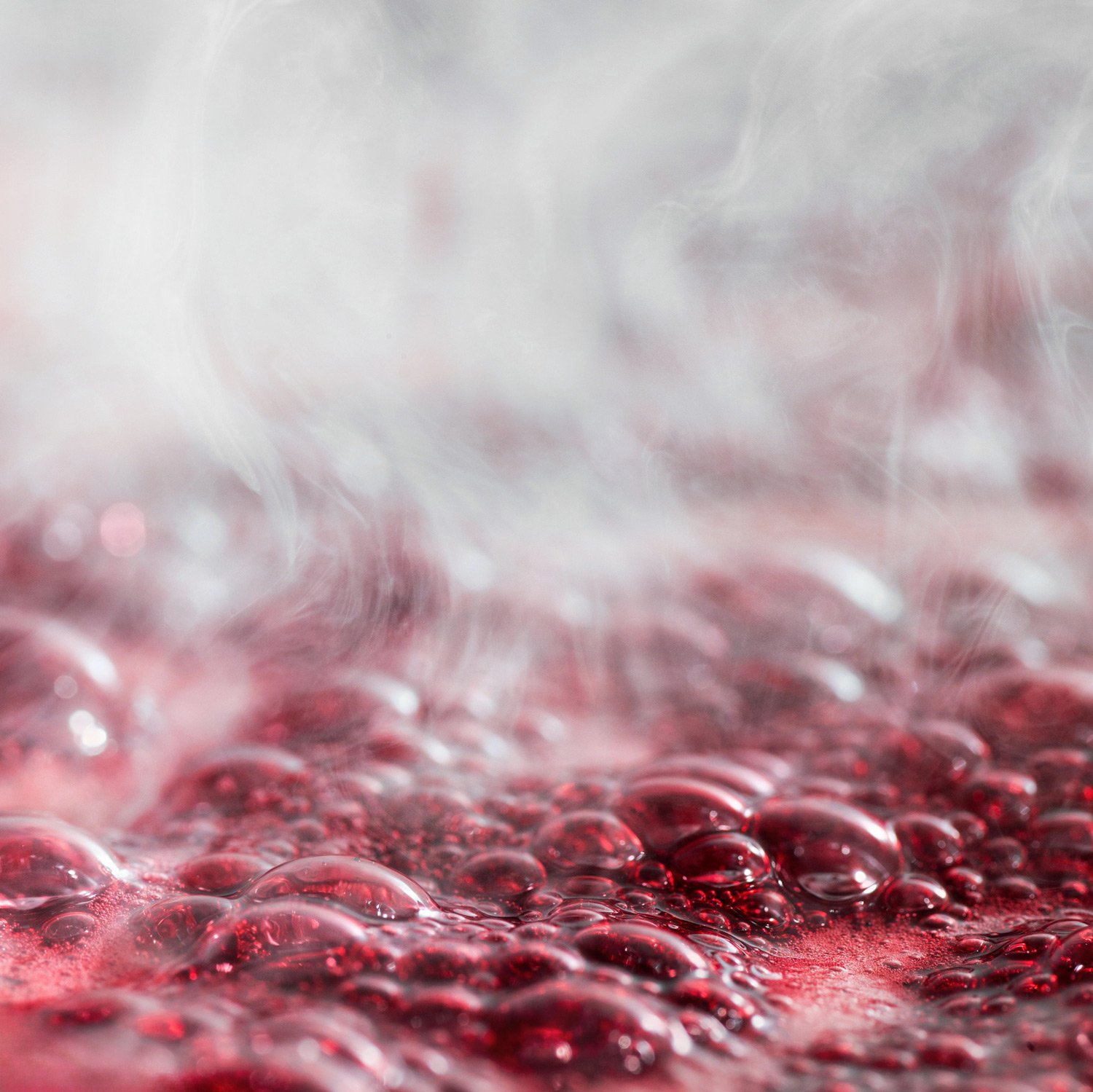 Close-up macro photography of boiling raspberries with steam and bubbles, capturing the artisanal process of making fruit coulis for pastry arts by Stavros Kostakis