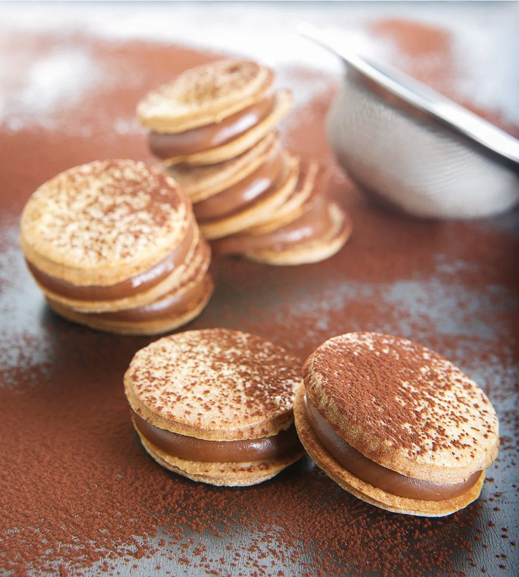 Artisanal chocolate biscuits filled with cream and dusted with cocoa powder, professional confectionery photography for bakery branding.