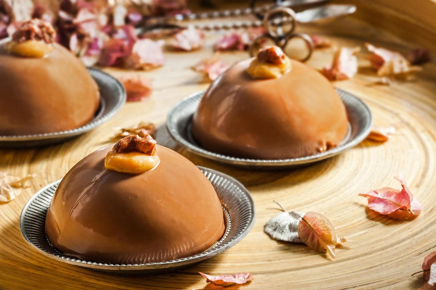 Professional pastry photography of chocolate mousse domes with caramel and walnuts on a wooden tray, captured by Stavros Kostakis. Editorial food styling and high-end confectionery lighting.