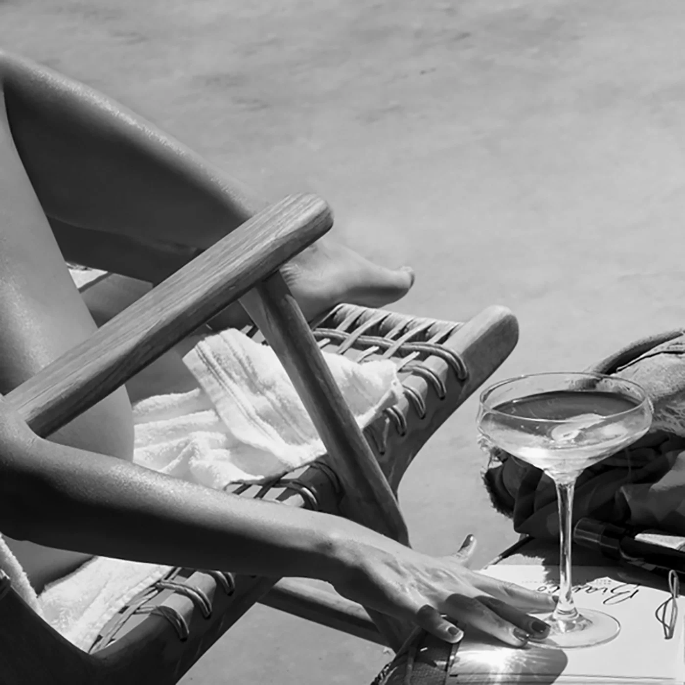 Luxury hospitality concept: Elegant black and white close-up photography of a guest holding a Martini cocktail at Bianco Beach House Tinos, emphasizing textures of the woven lounger and the serene Aegean lifestyle, captured by Stavros Kostakis.