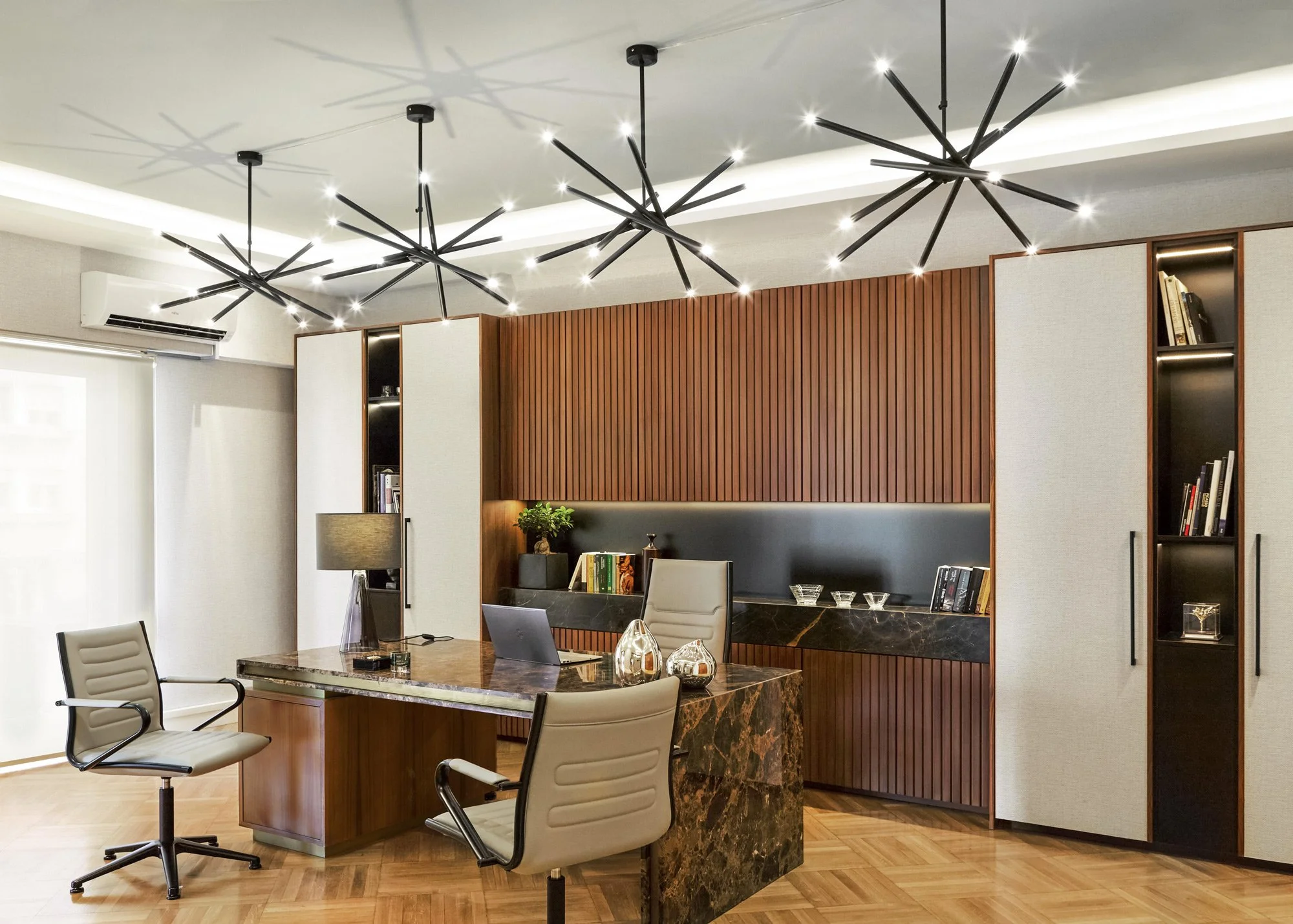 Wide-angle professional photography of an executive office in Kolonaki. Features custom wood paneling, starburst-style chandeliers, and bespoke office furniture designed by Sissy Feida.