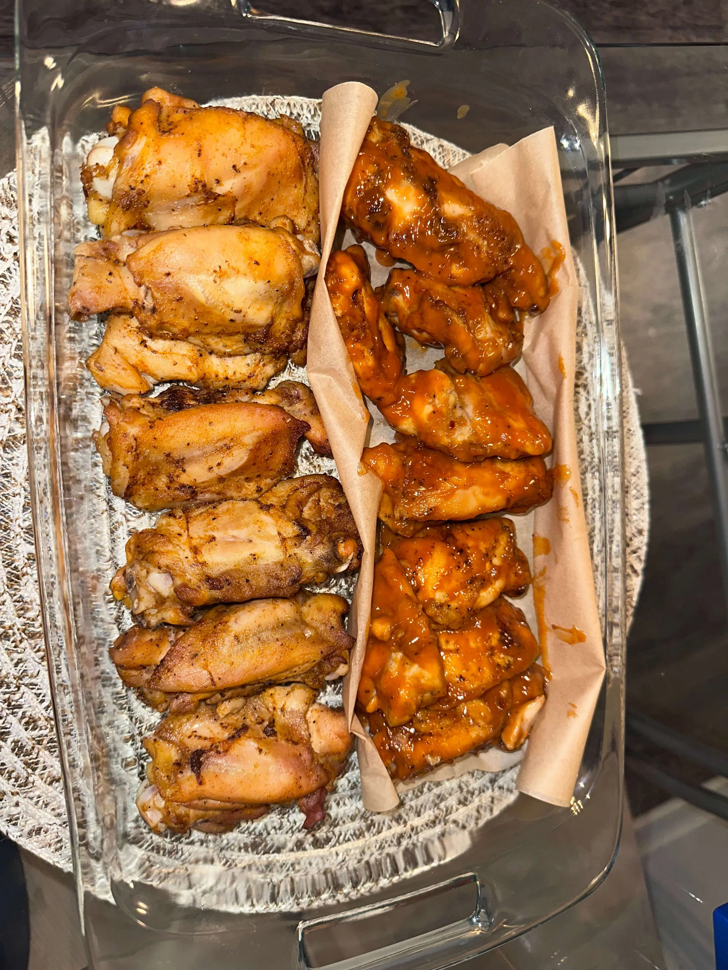 A glass serving dish with fried chicken pieces on the left and sauced chicken wings on the right, separated by a paper divider.