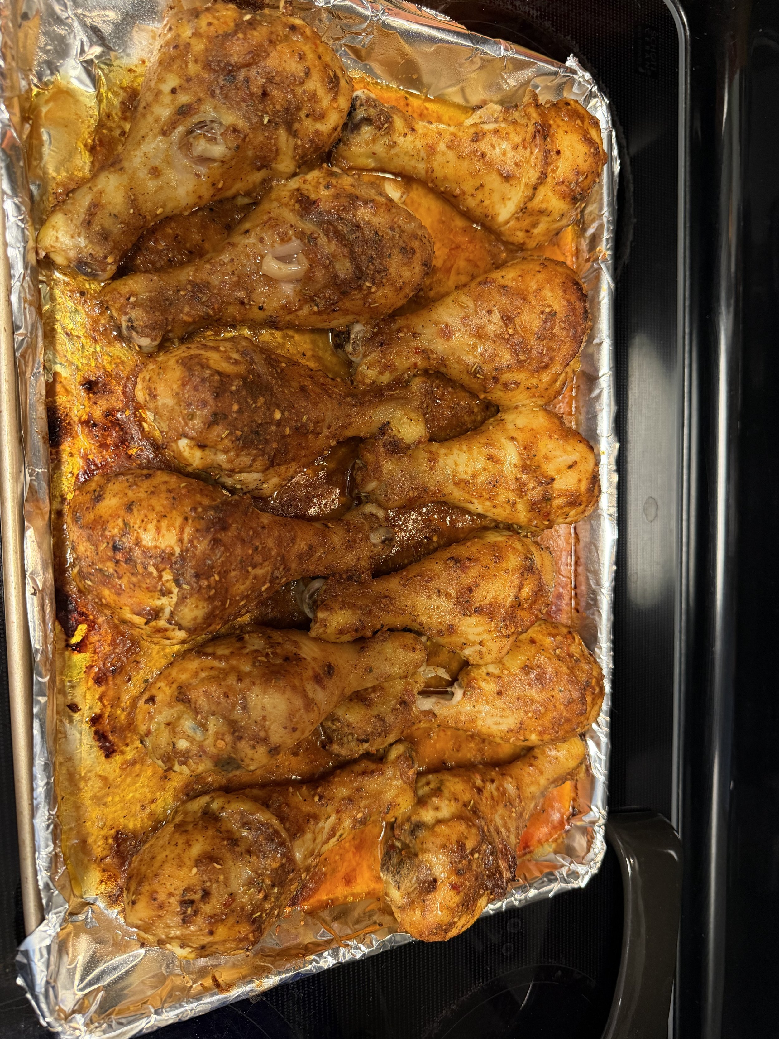 Baked chicken drumsticks seasoned with spices on a foil-lined baking sheet.