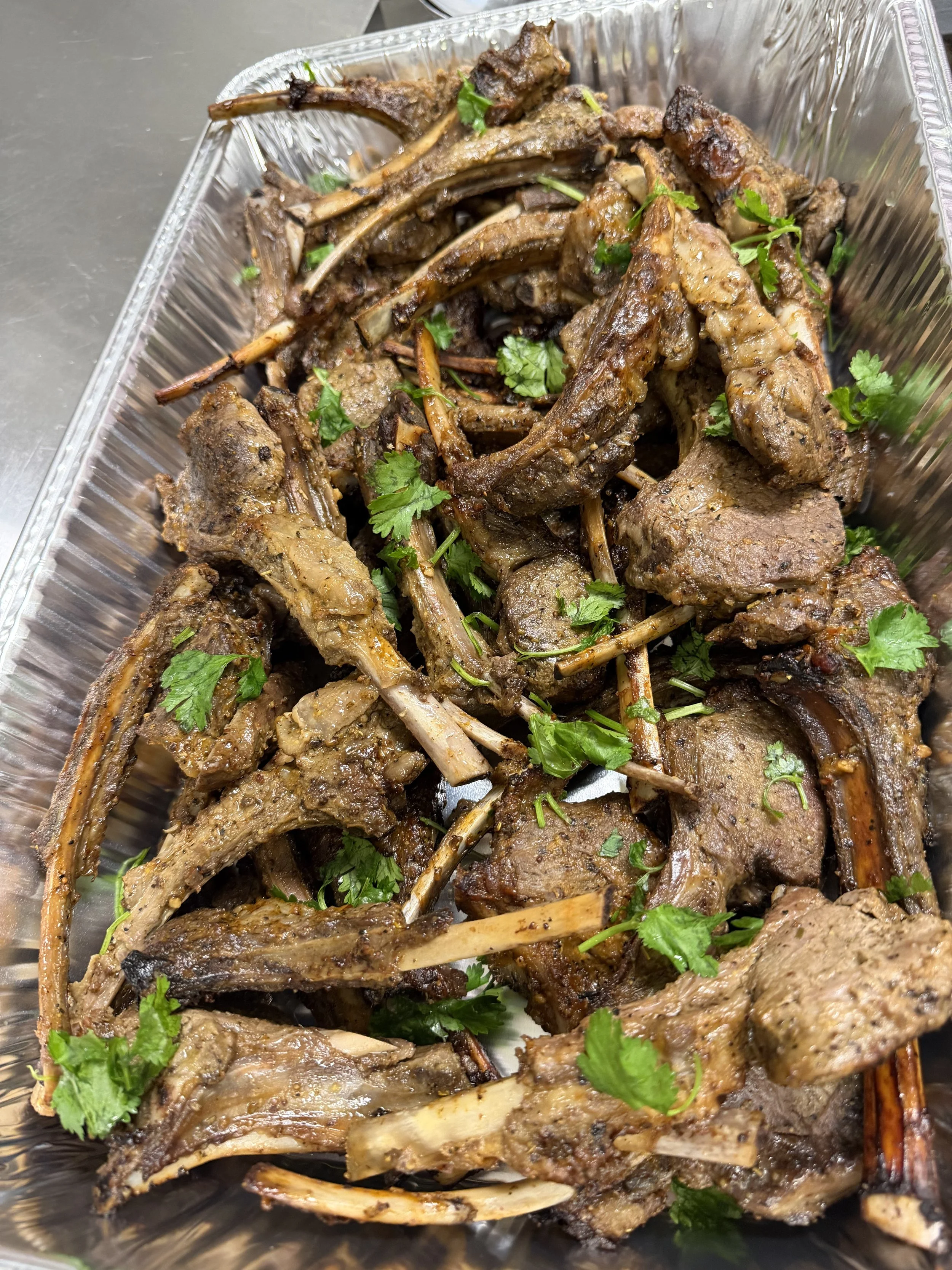 A tray of cooked lamb chops garnished with fresh cilantro.