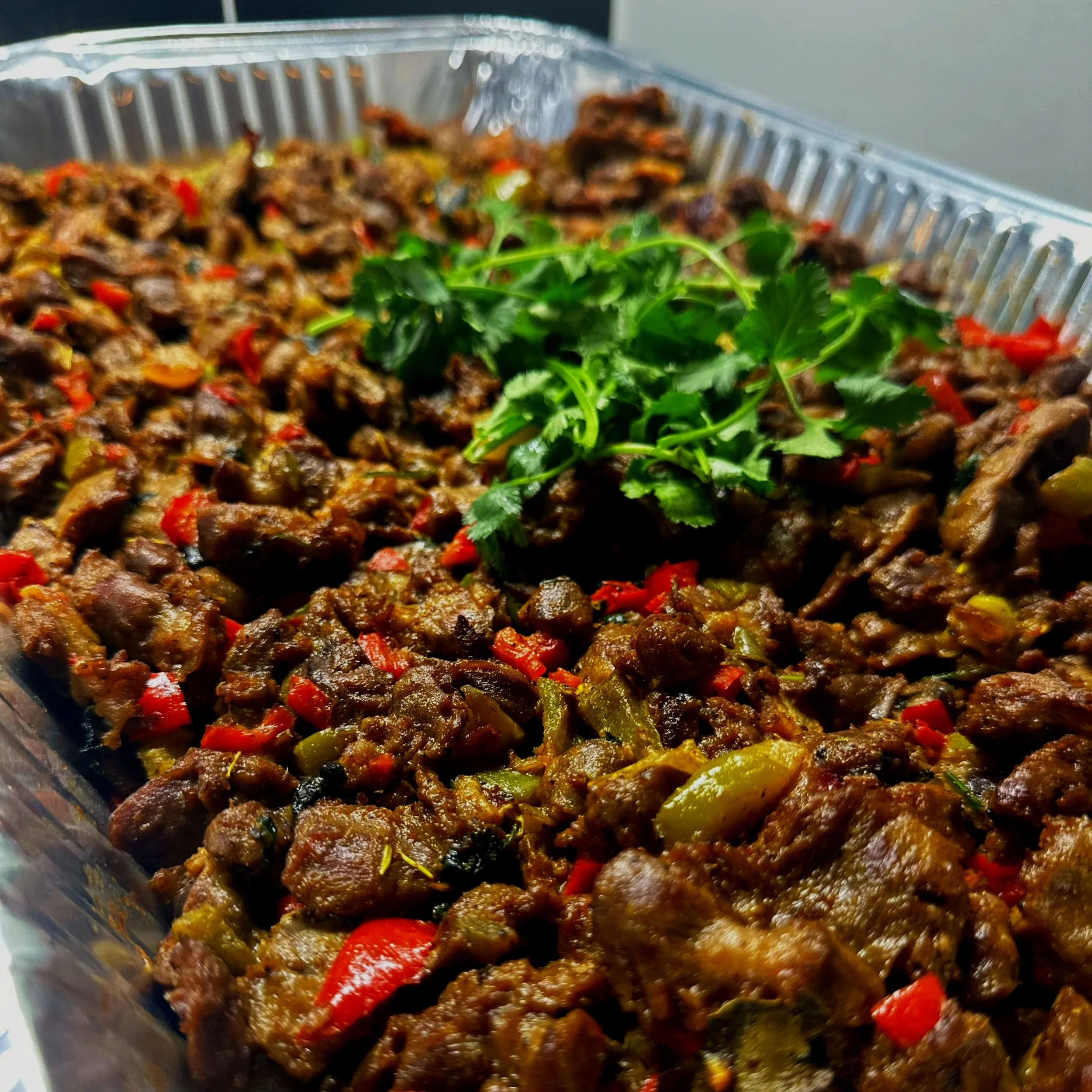 Close-up of cooked beef stir-fry with red and green peppers, garnished with fresh cilantro, in a takeout container.