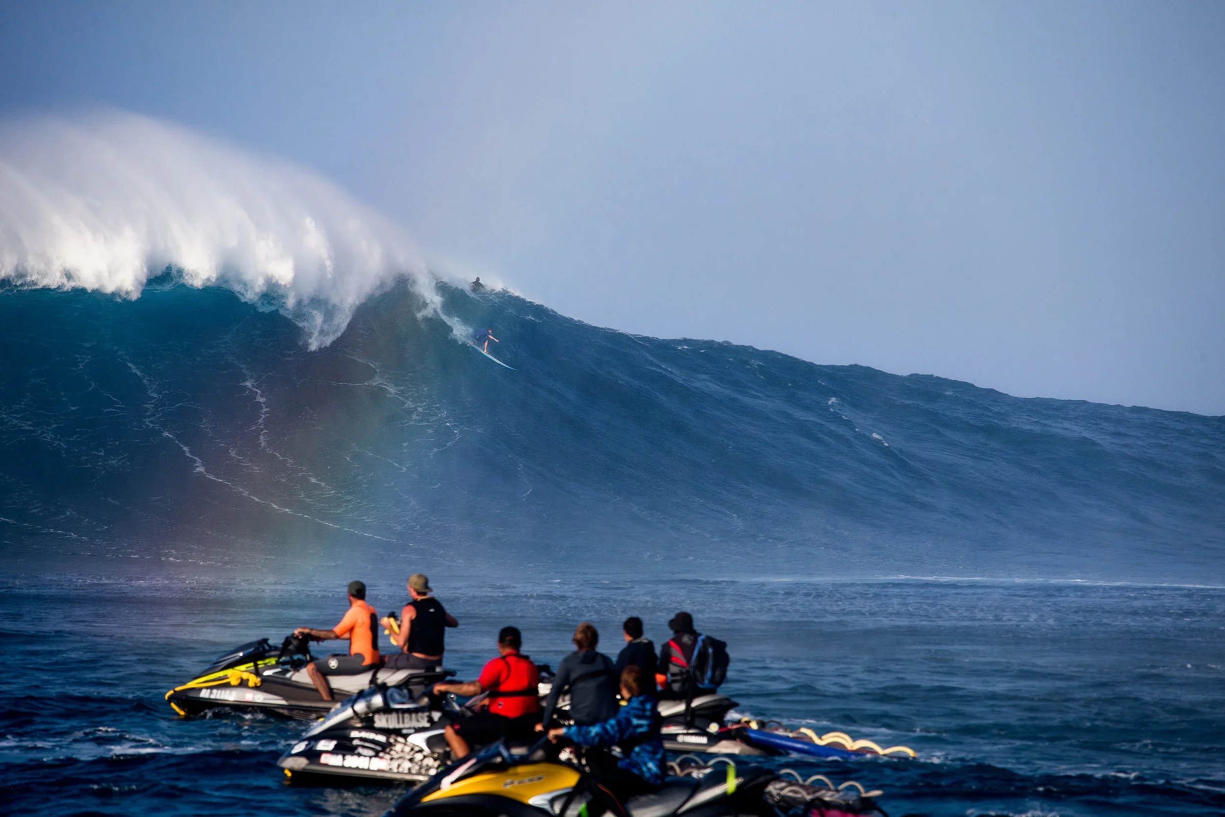 Mark Visser paddling into a huge wave at Jaws, Pe'ahi, with a rainbow and jet ski spectators watching