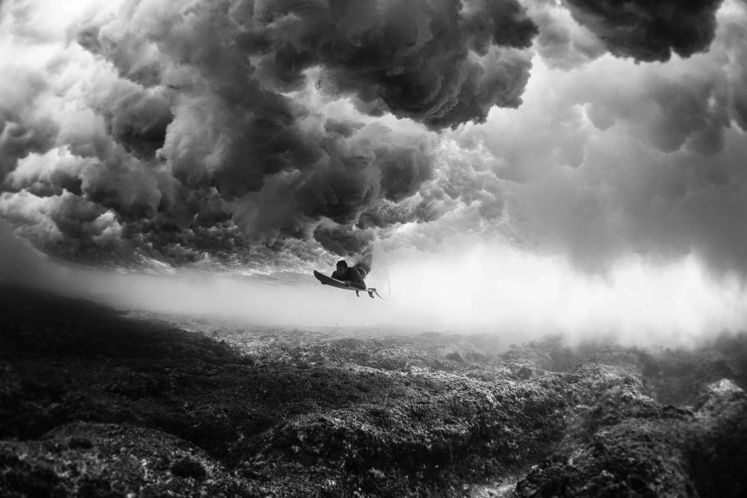 Black and white underwater image of Mark Visser duck diving under a wave at Cloudbreak, Fiji
