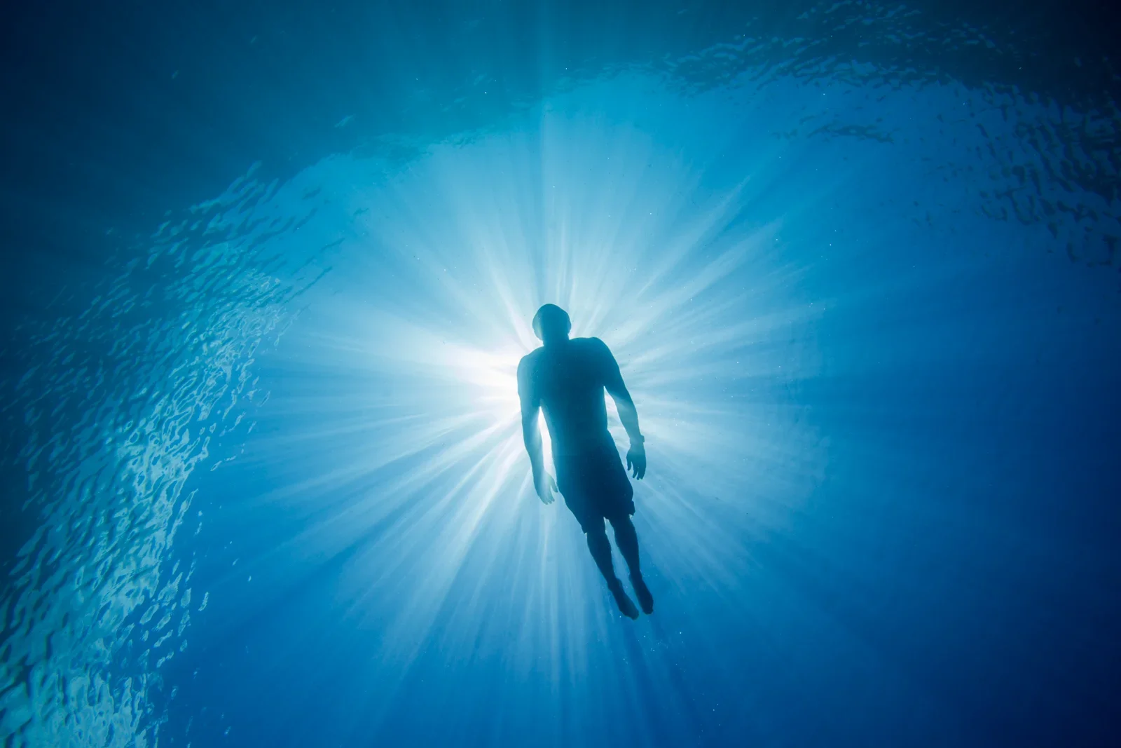 Mark Visser breath-hold training at Namotu Island, Fiji. Silhouette of Mark Visser  swimming underwater with rays of light shining from above.
