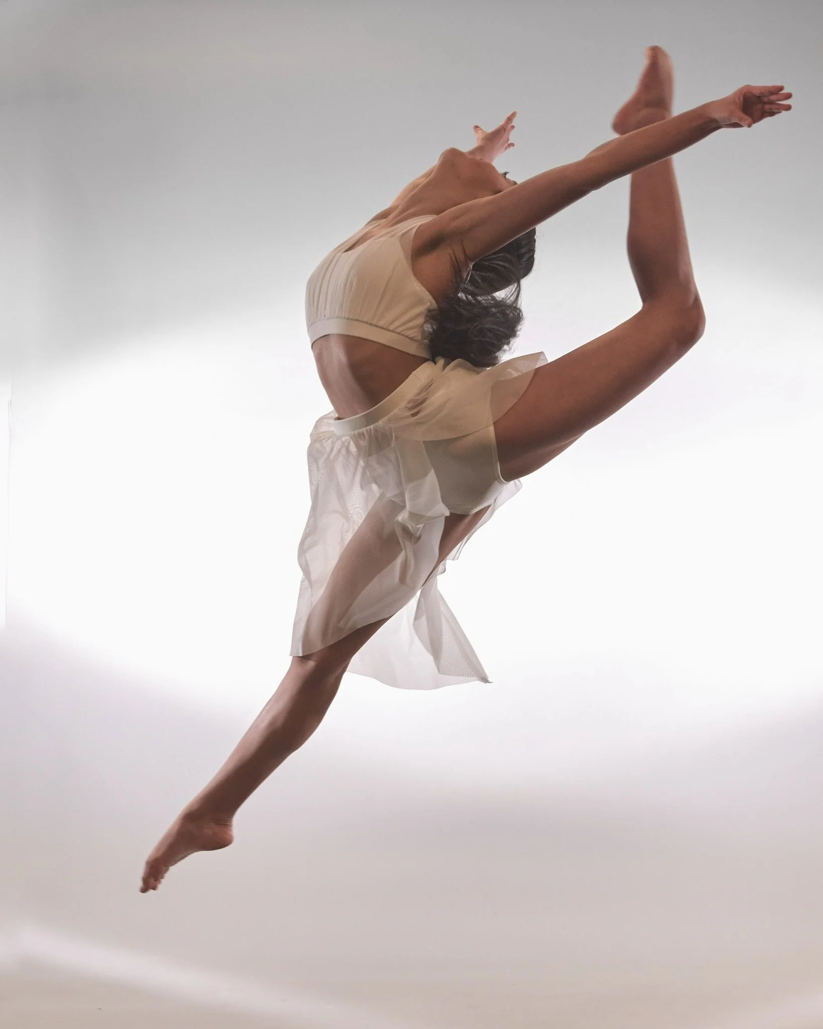 A dancer performing a backbend with arms extended and one leg raised, against a soft, gradient background.