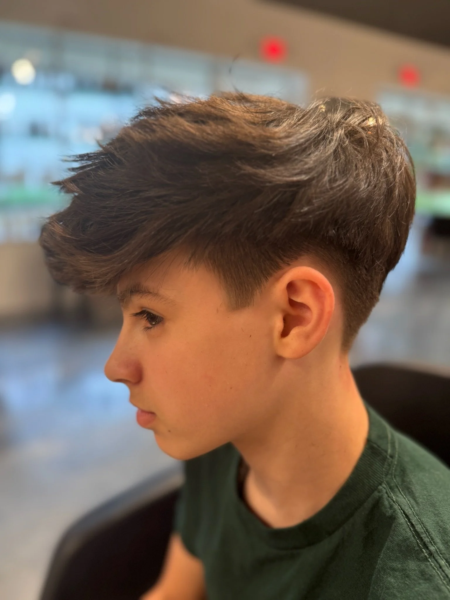Close-up of a young person's side profile with short, styled brown hair and wearing a green shirt.