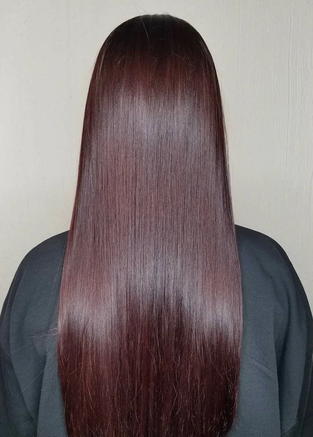 Back of a person with long, wavy, reddish-brown hair wearing a black shirt outdoors on a sunny day.