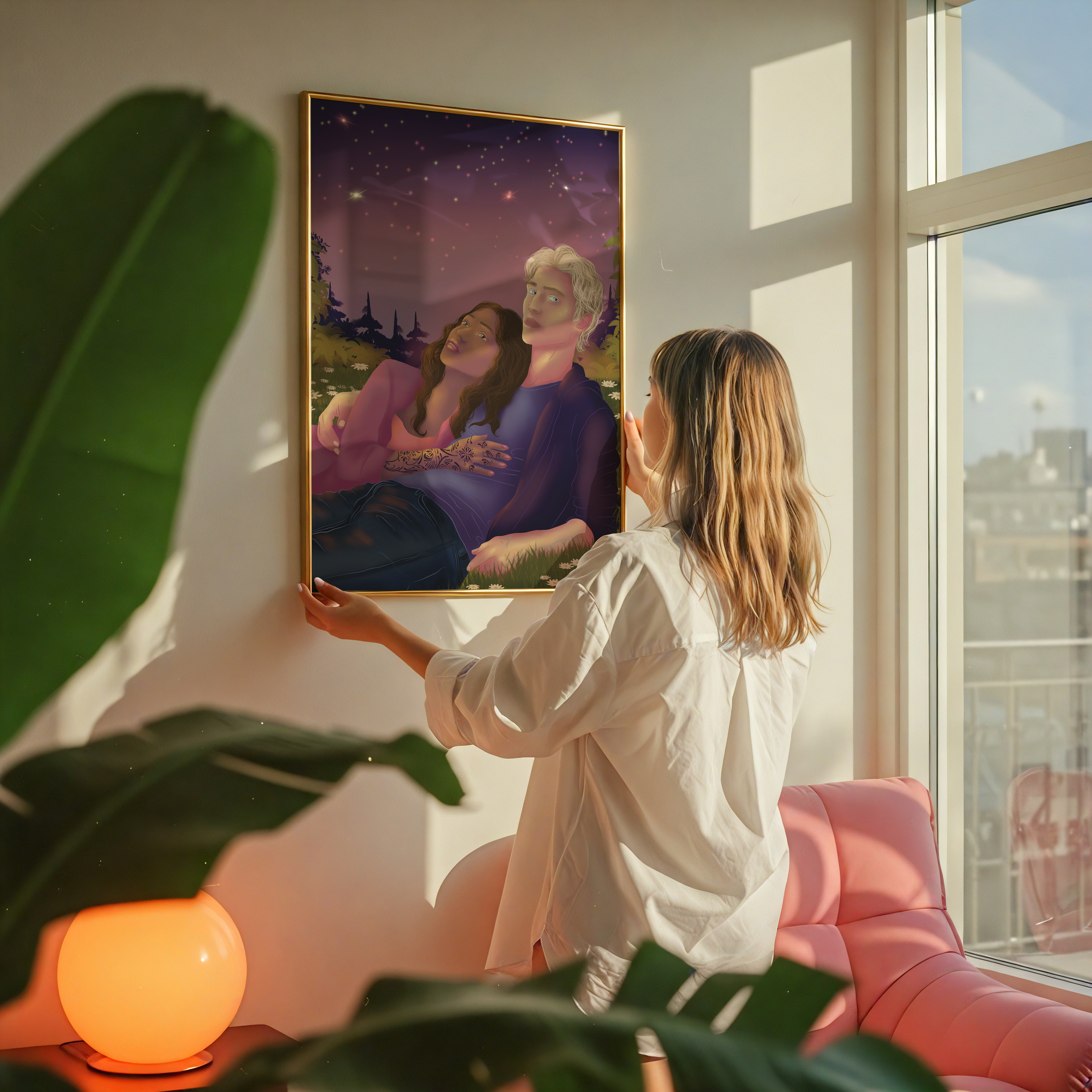 A woman with blonde hair in a ponytail is looking at a digital art painting of a man and woman in a nature scene under a starry sky on a white wall in a brightly lit room. The room has large windows with daylight outside, and there are large orange spherical lamp and a pink sofa.