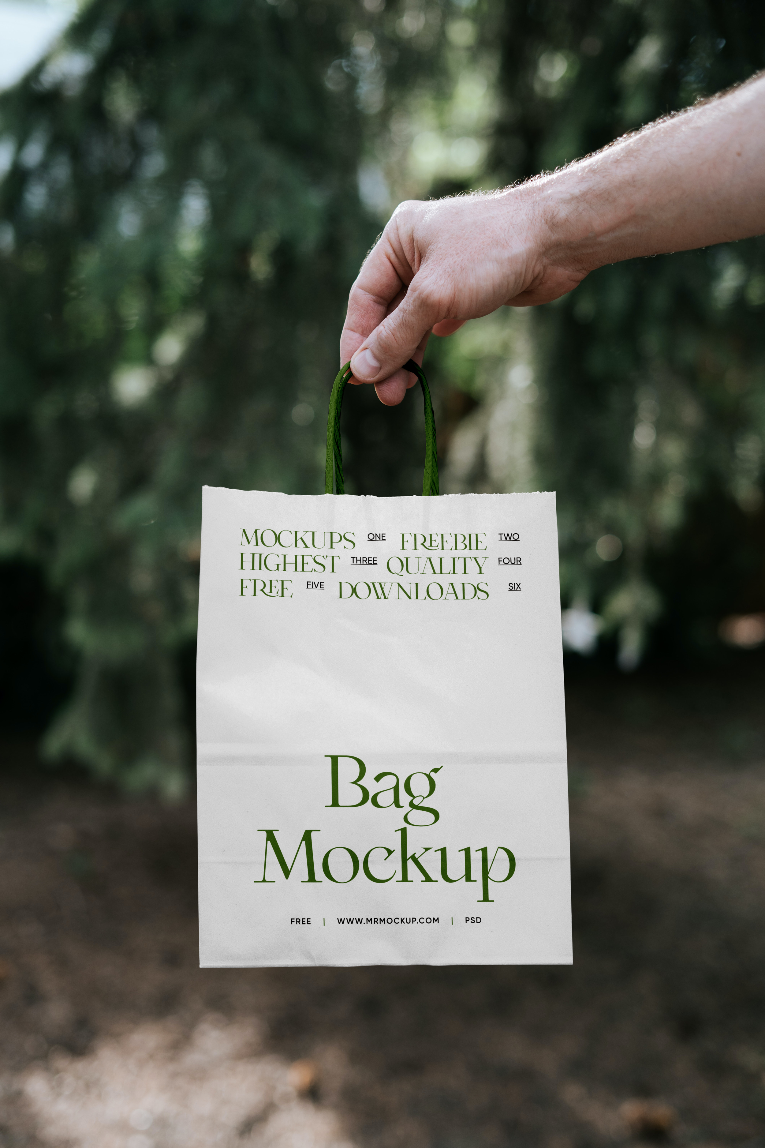 A hand holding a white shopping bag with green handles in an outdoor setting with blurred trees and greenery in the background.