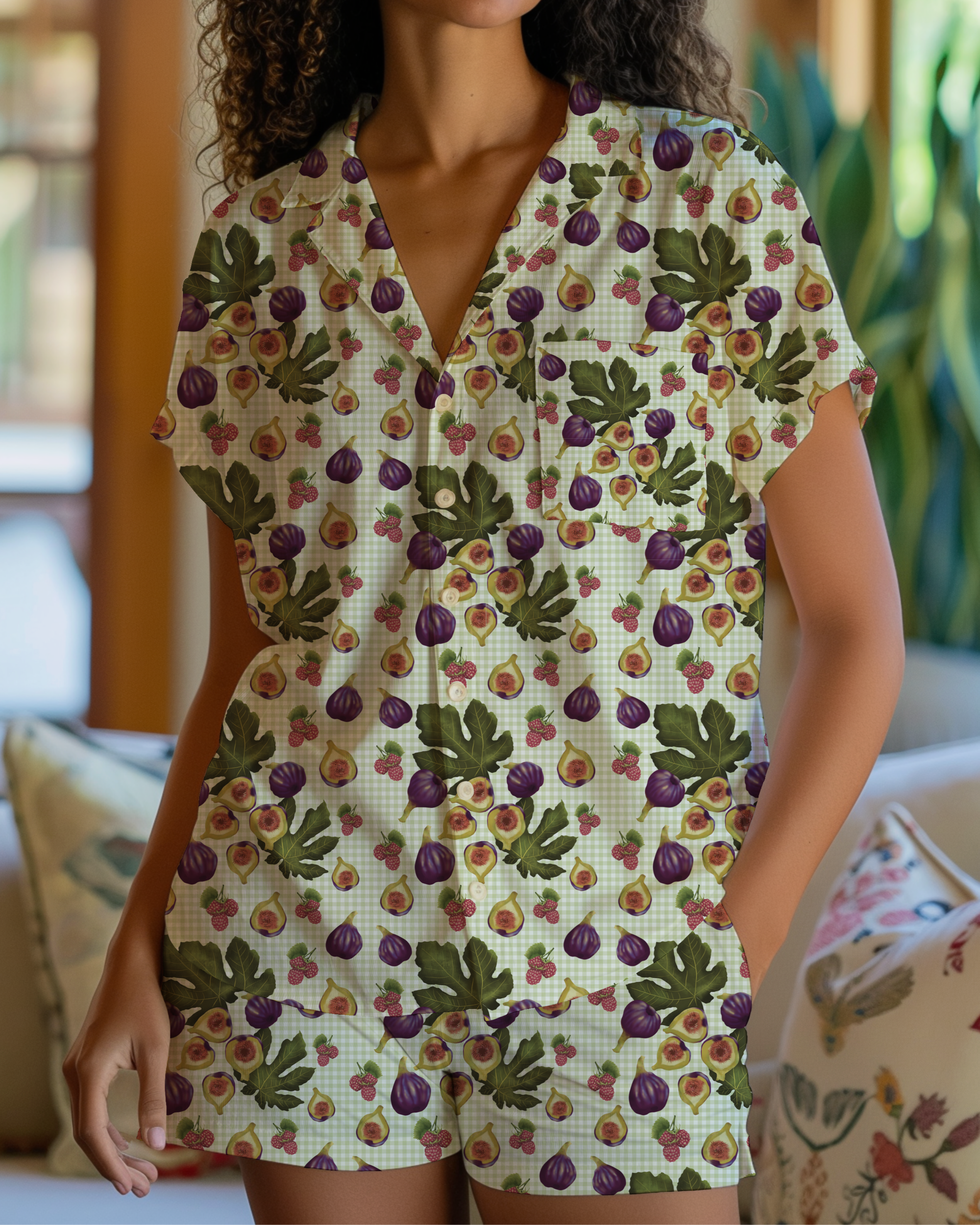 Person in a cream-colored short-sleeve button-up shirt and matching shorts, standing indoors with greenery in the background.