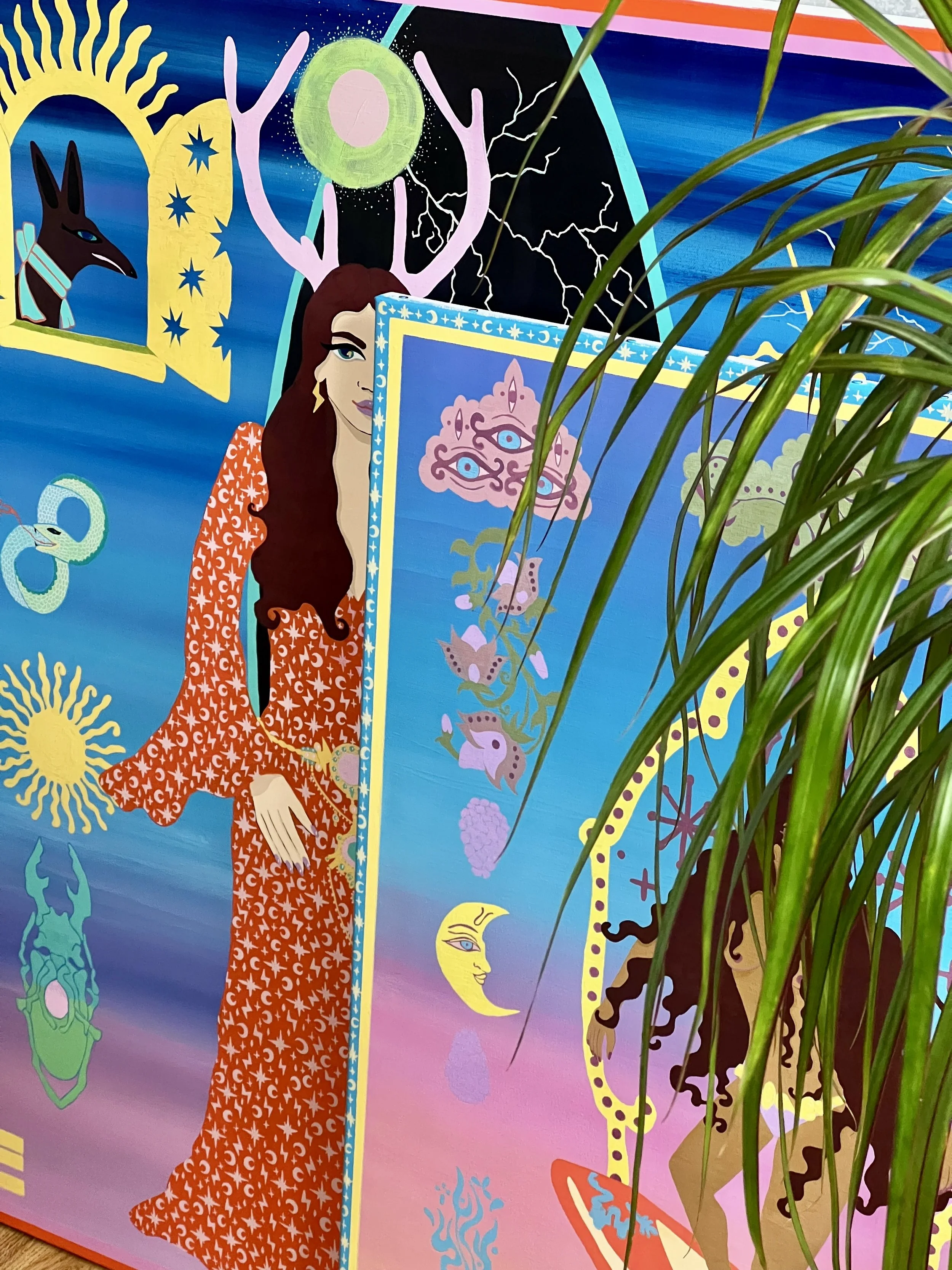 Colorful fantasy mural featuring a woman with long brown hair, a deer with antlers, a green snake, a smiling crescent moon, a face in a cloud, and various celestial and animal imagery with vibrant background.