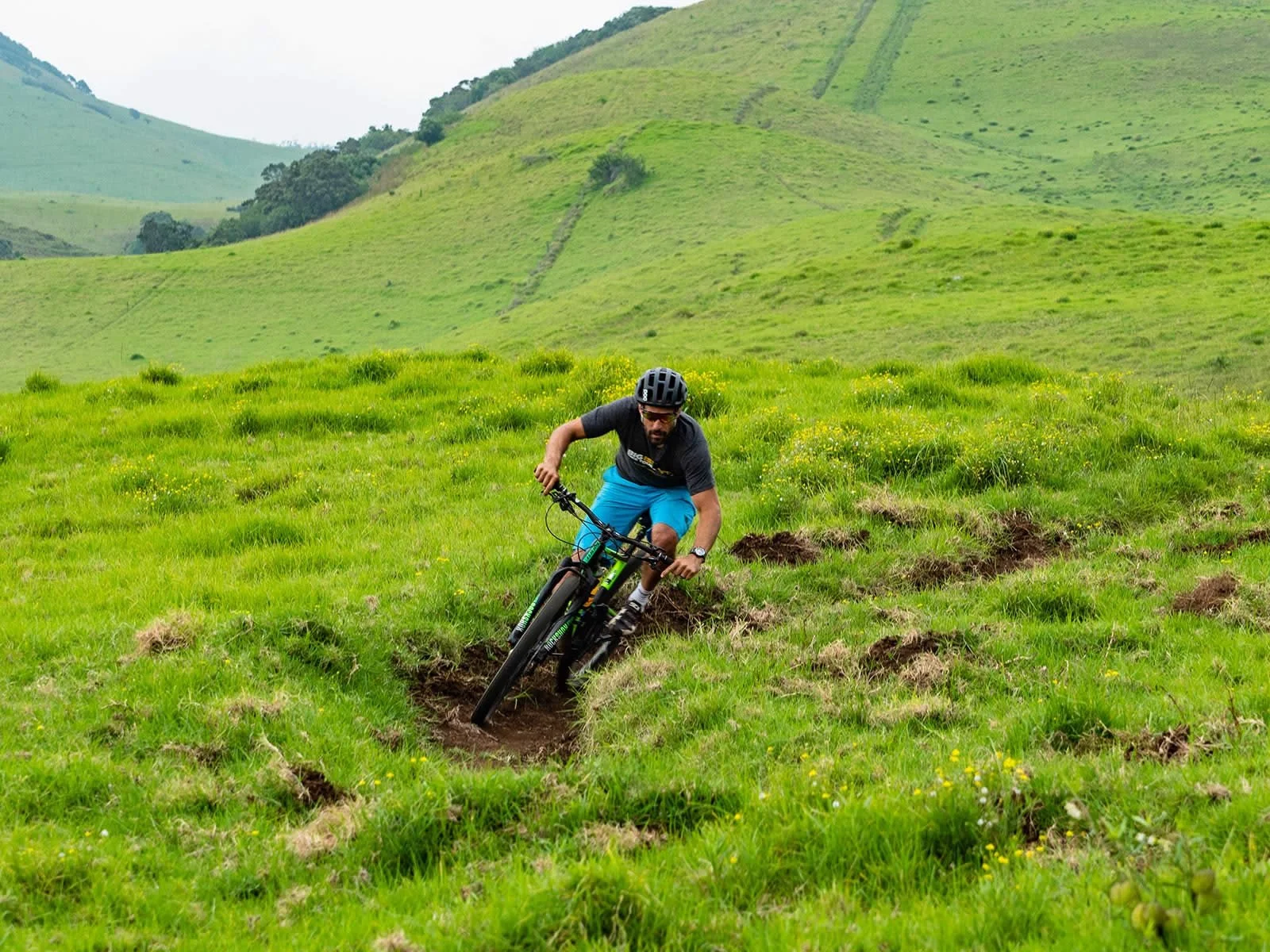 A man riding a mountain bike on a grassy trail through rolling green hills.