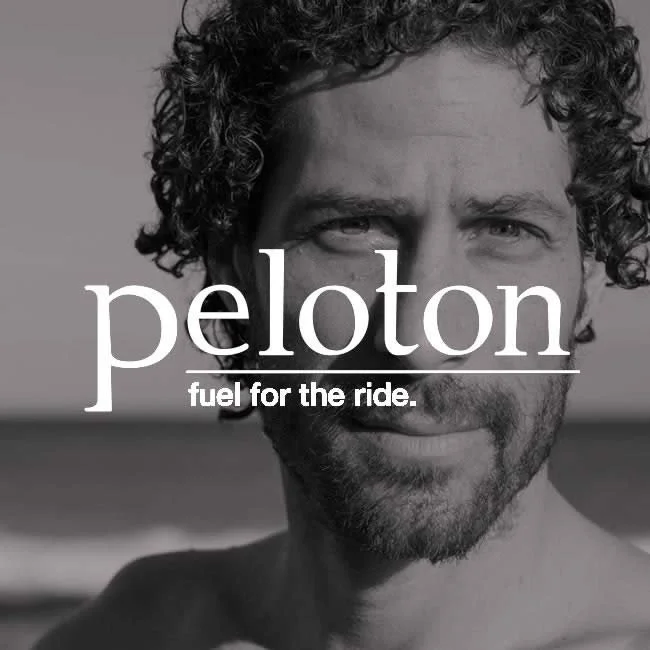 Close-up black-and-white photo of a smiling man with curly hair and a beard, with the Peloton logo and the slogan "fuel for the ride." overlaid.