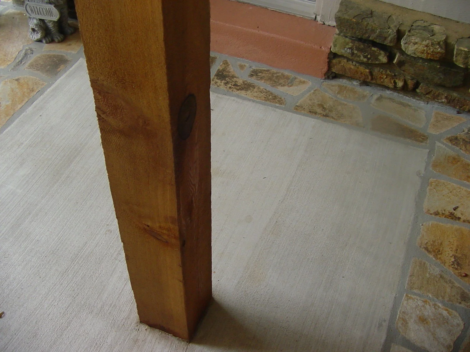 A close-up of a wooden door frame with a brown finish, next to a brick wall with a mix of tan, brown, and gray stones, and a painted concrete floor.