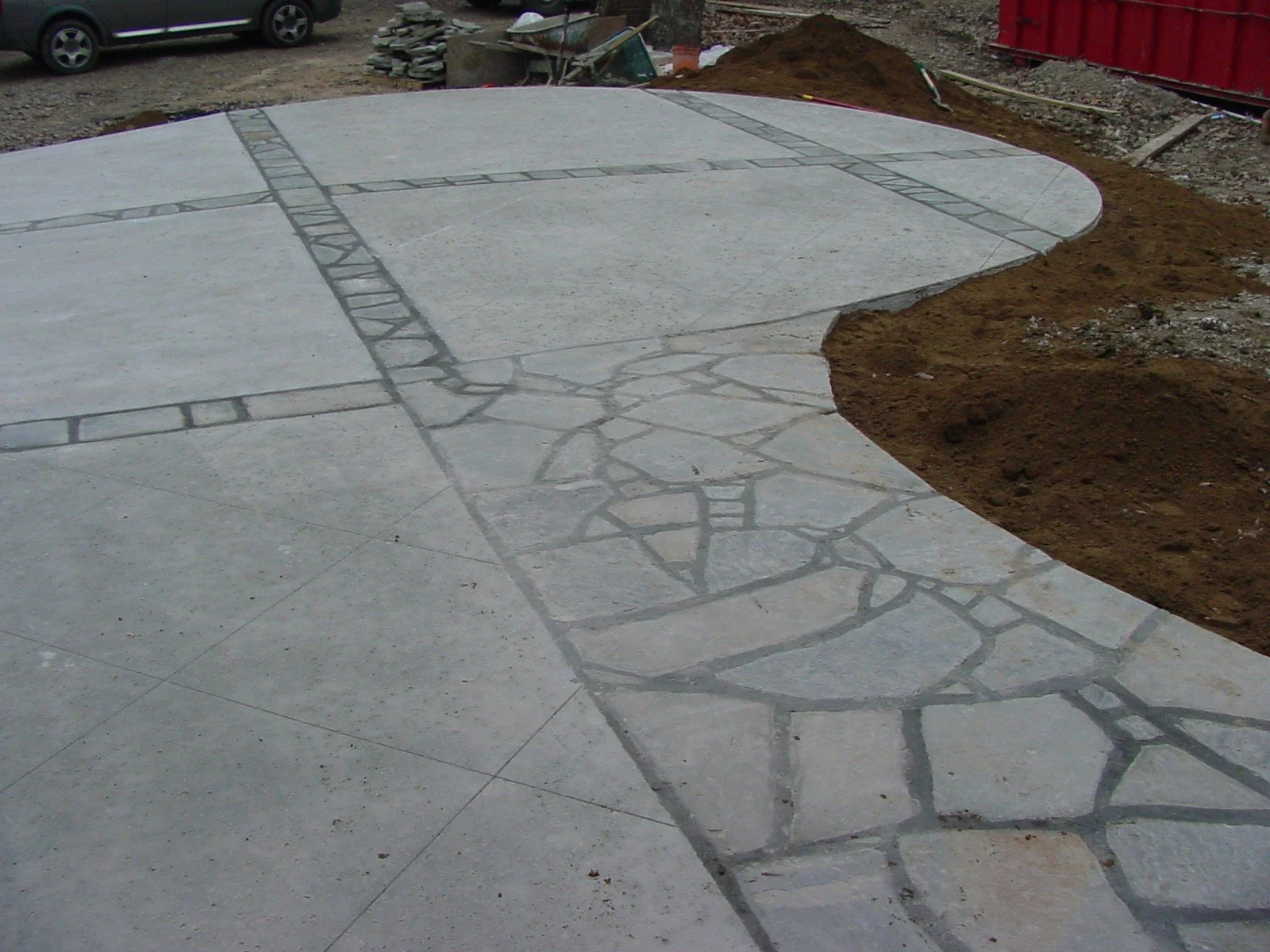 Concrete sidewalk with decorative inlay, construction site background with dirt, tools, and a parked vehicle.