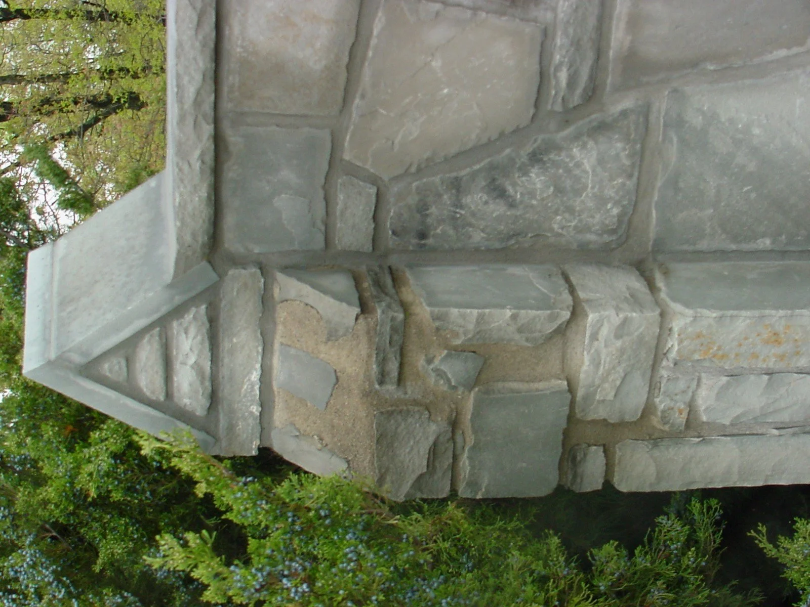 Close-up of a stone corner with a decorative water spout in a stone wall, surrounded by greenery.